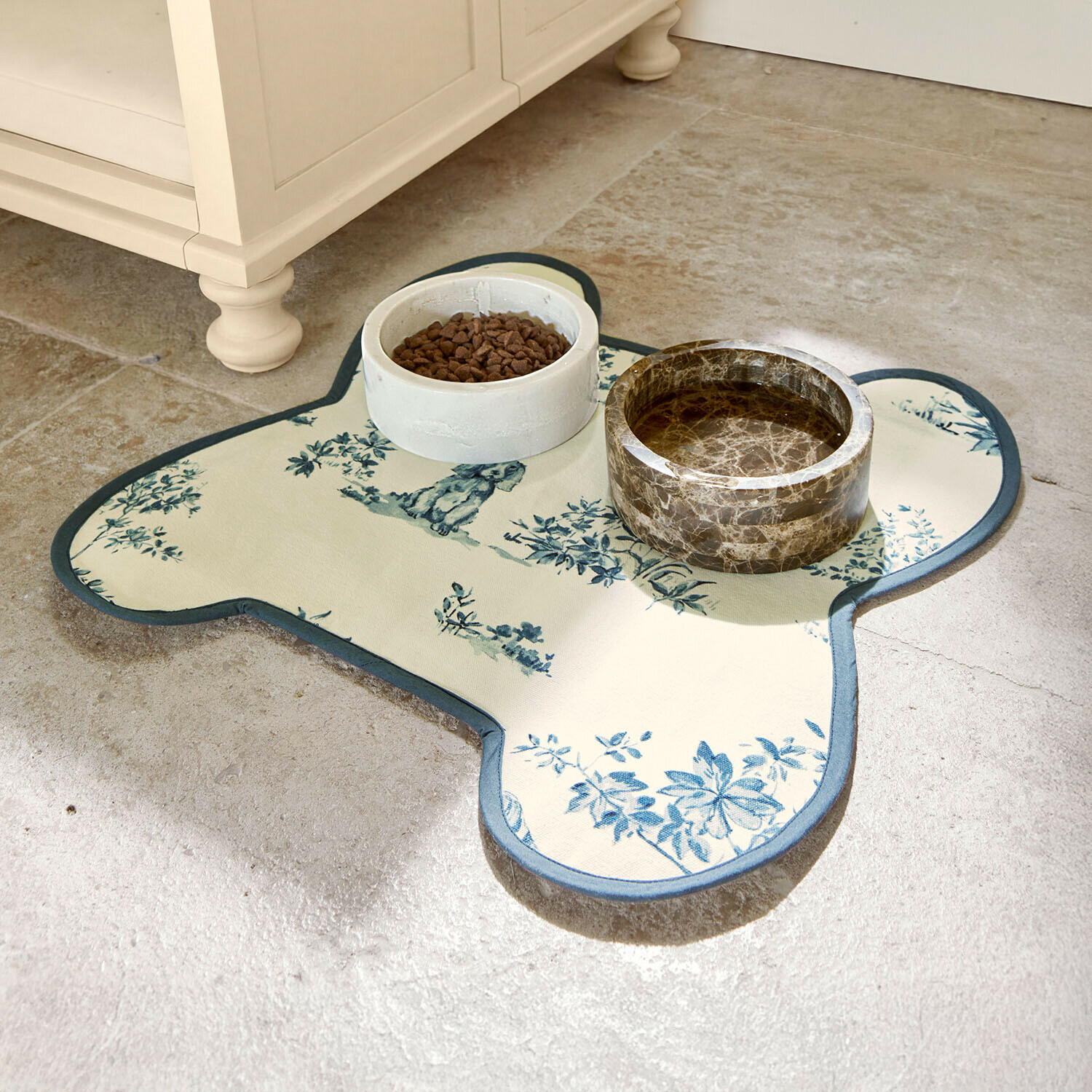 Tapis pour gamelles avec motif floral bleu sur fond crème, accompagné de bols en céramique pour animaux