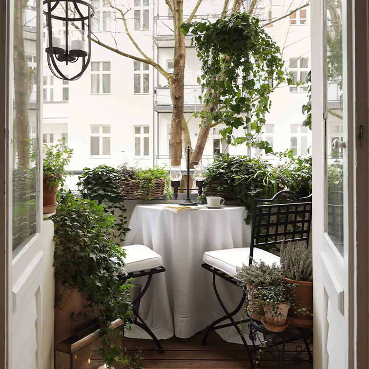 Balcon cosy avec table ronde blanche, chaises noires et plantes vertes en pots décoratifs