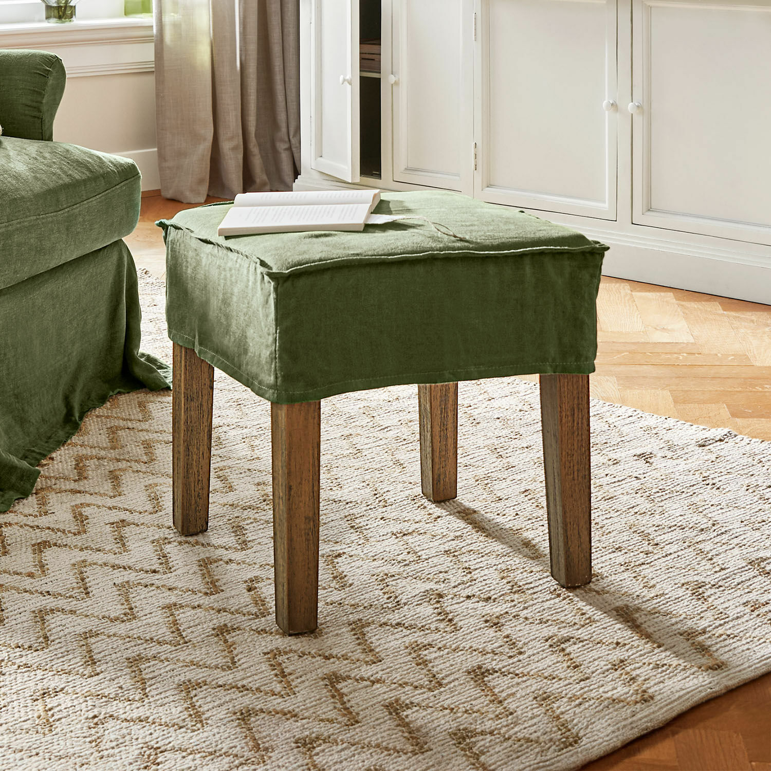 Tabouret Vionnique Repose-pieds vert en tissu lin avec pieds en bois sur tapis clair dans un salon lumineux