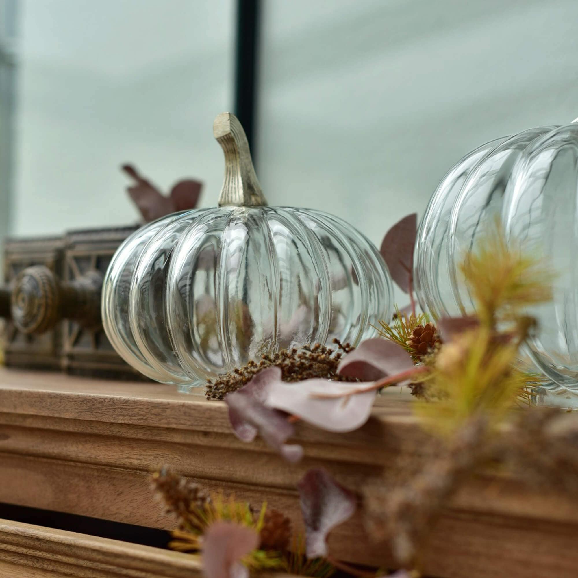 Citrouille en verre transparent avec tige beige sur surface en bois décorée d'éléments d'automne