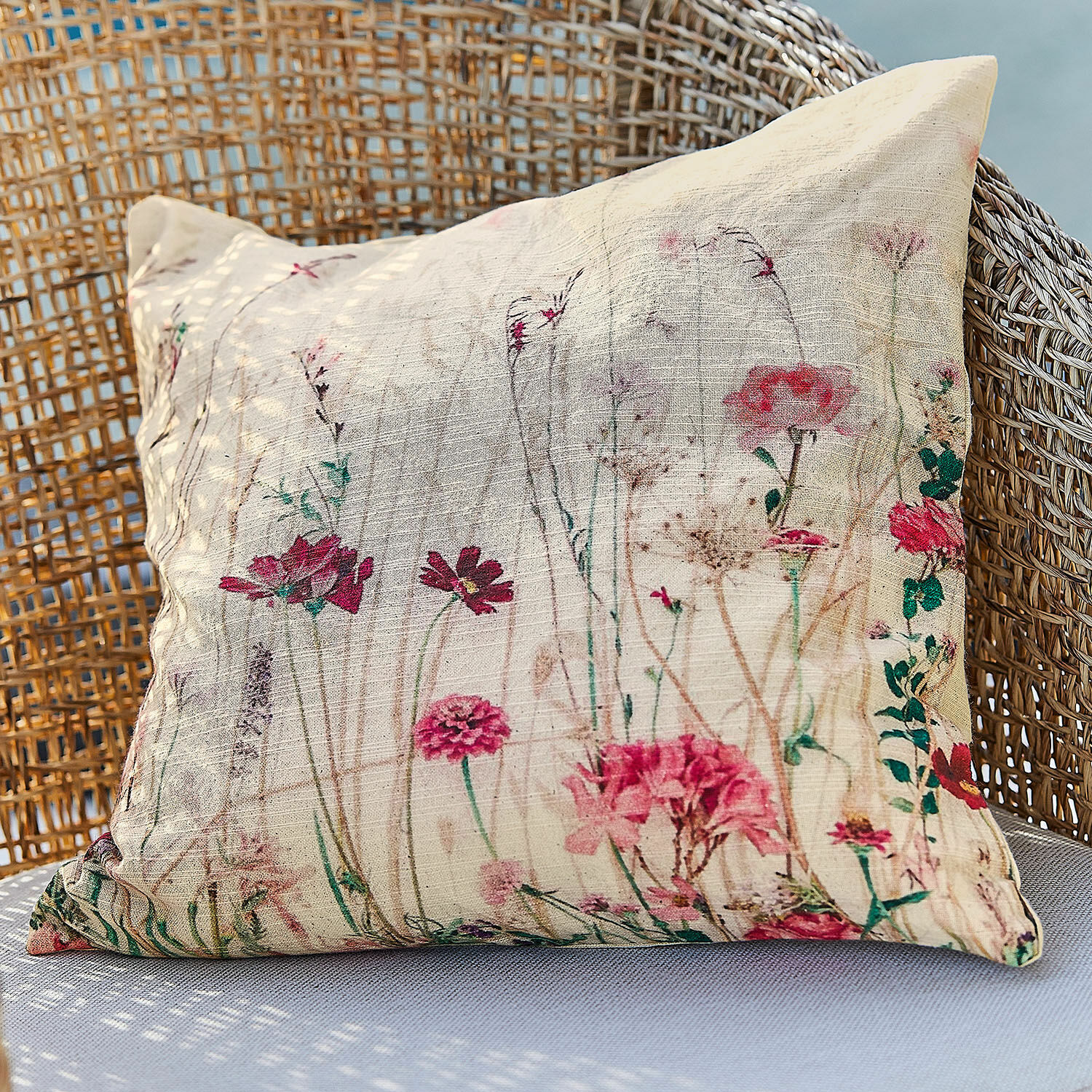 Housse de coussin Briovene Coussin beige en tissu naturel avec imprimé floral posé sur un fauteuil en osier, décoration intérieure