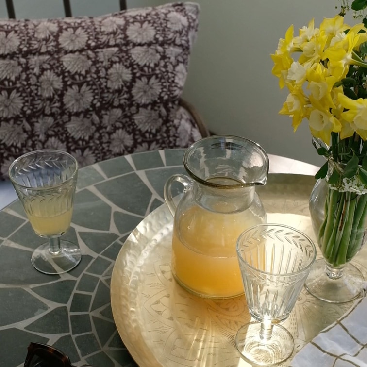 Carafe en verre avec boisson jaune et deux verres sur table en marbre avec fleurs en vase