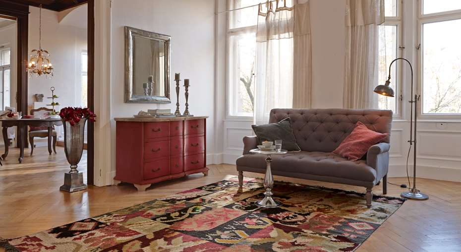 Salon style French chic avec canapé gris capitonné, buffet rouge en bois et tapis coloré