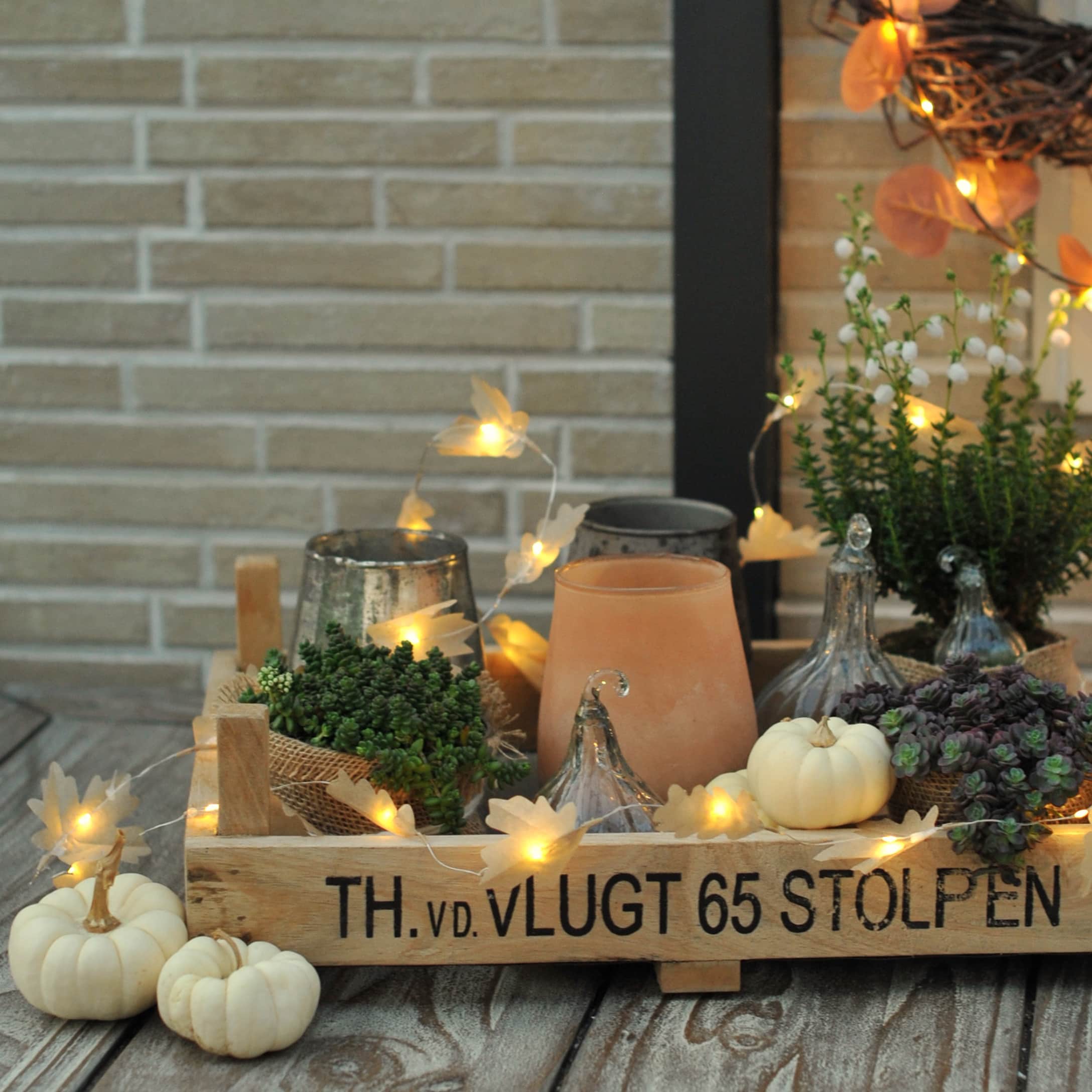 Caisse en bois avec décorations d'automne, petites citrouilles blanches, plantes et guirlande lumineuse LED