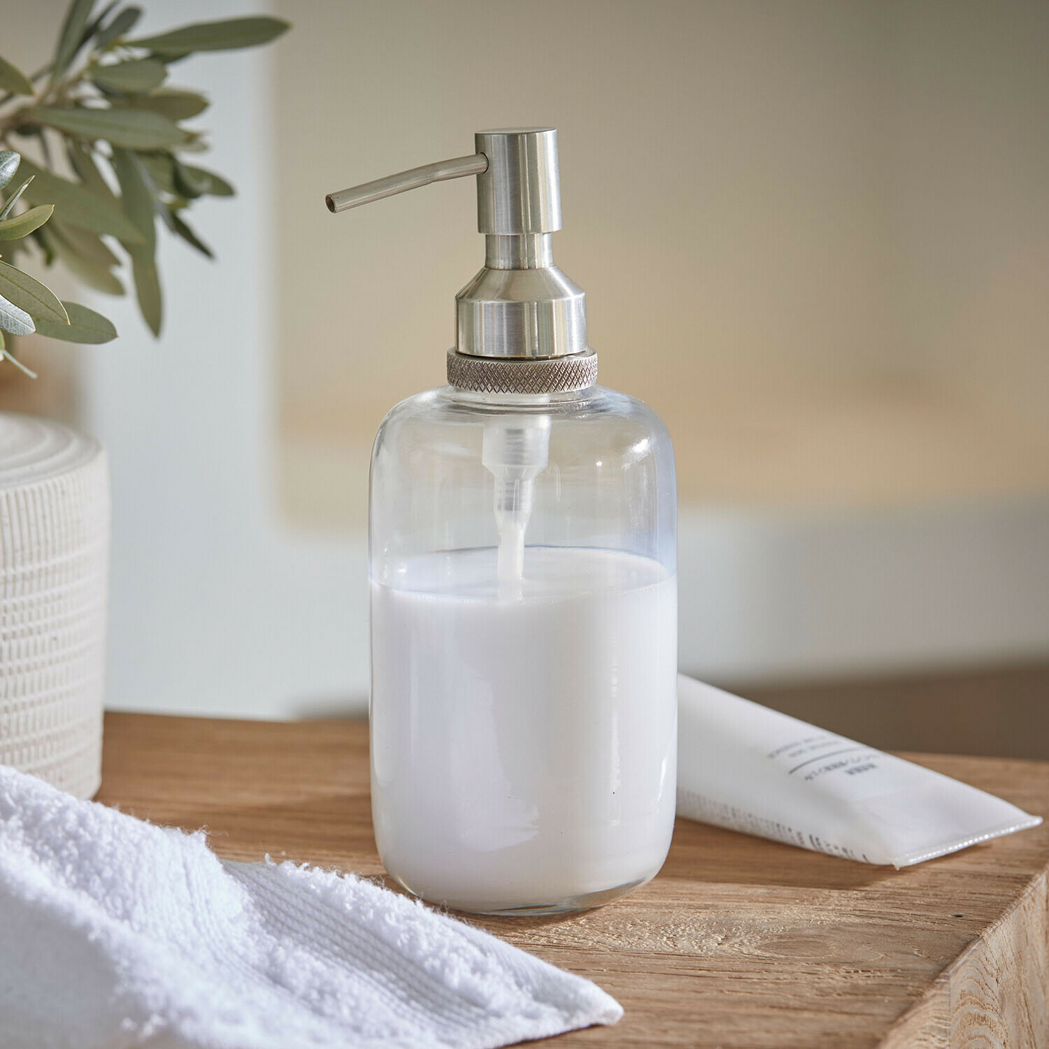 Distributeur de savon Linsted Distributeur de savon transparent en acier inoxydable avec liquide blanc sur surface en bois