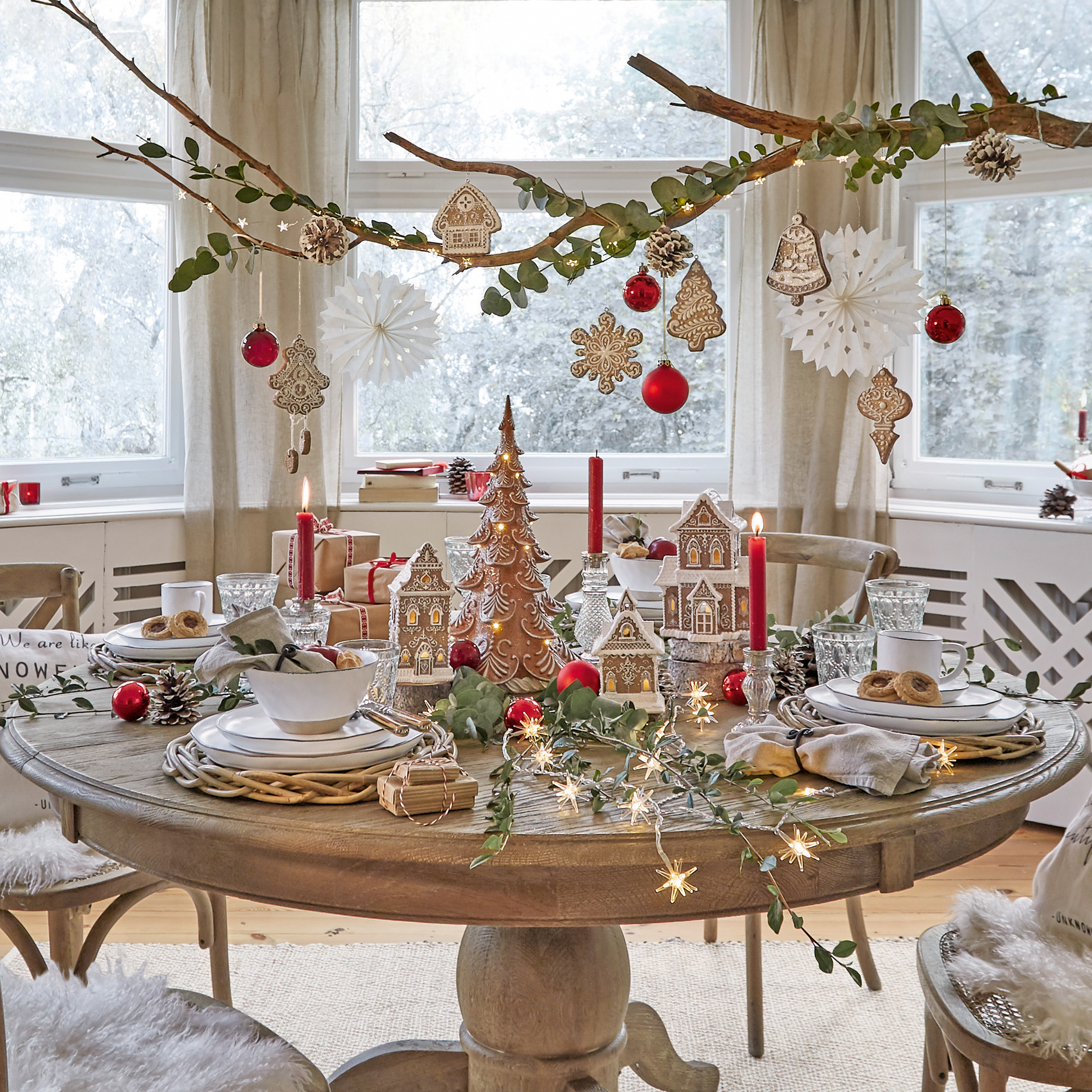 Table en bois décorée pour Noël avec maisons en pain d'épices, boules rouges et bougies allumées