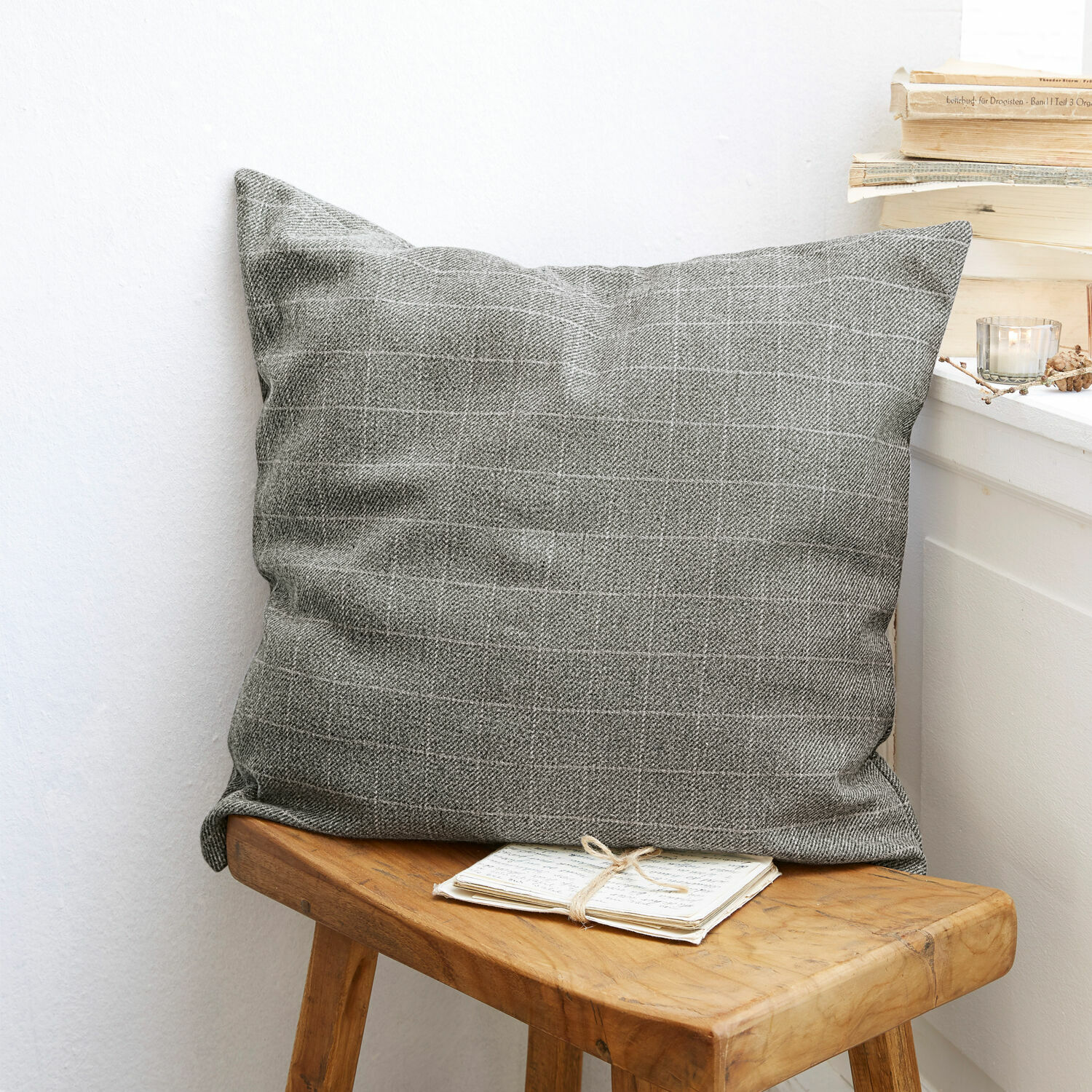Housse de coussin Dublanc Coussin décoratif gris à motif quadrillé posé sur un tabouret en bois dans un intérieur cosy