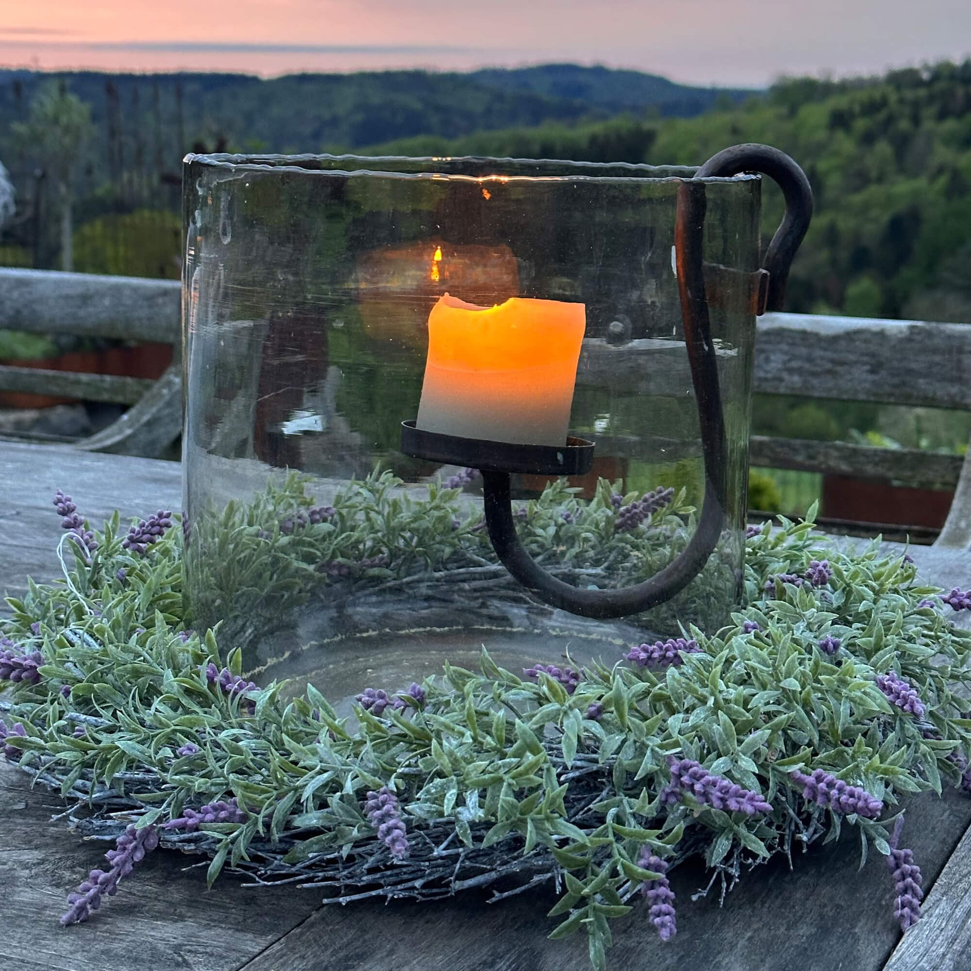 Photophore en verre avec support en métal et couronne verte à fleurs violettes sur table en bois