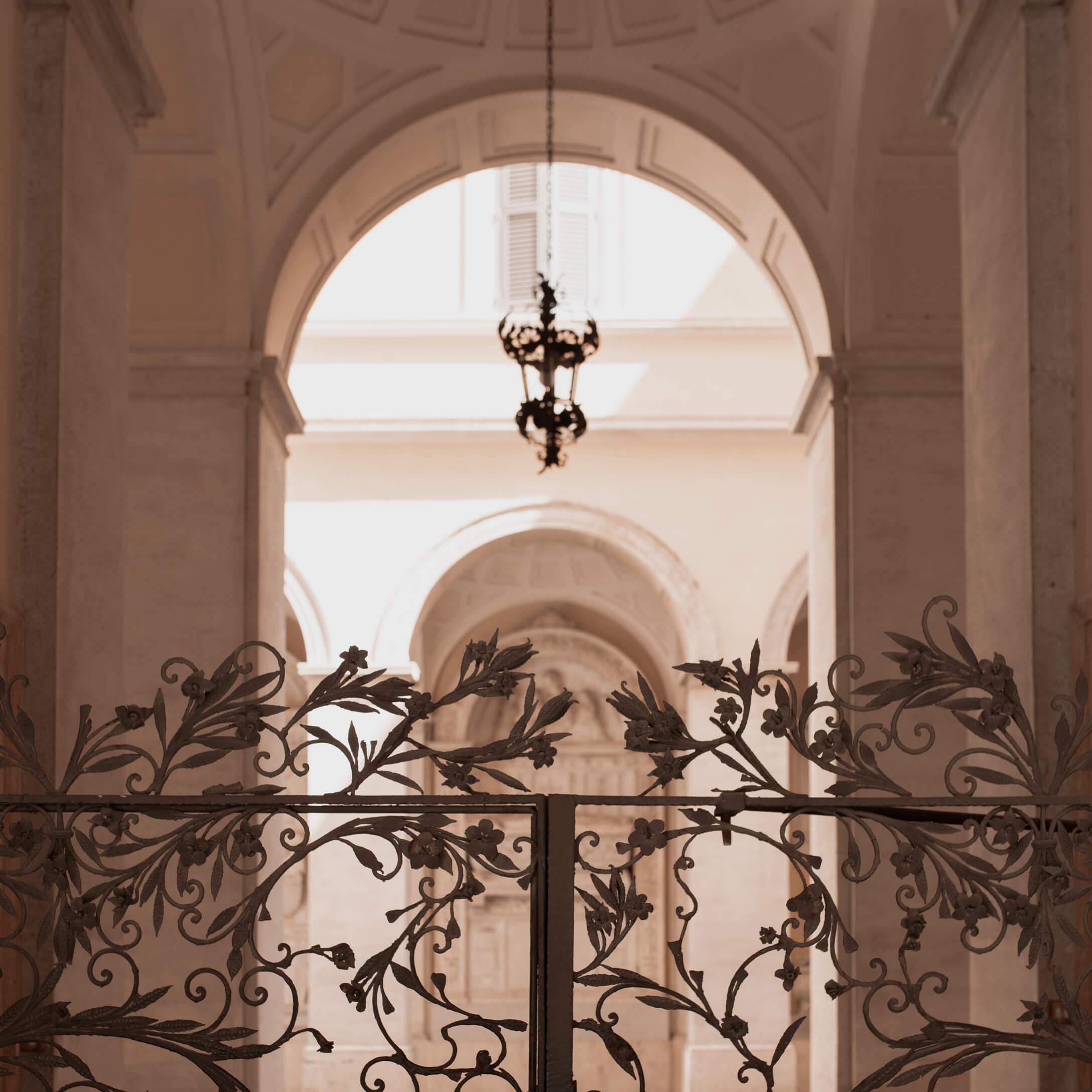 Portail en fer forgé orné de motifs floraux devant une arche lumineuse avec une lampe suspendue