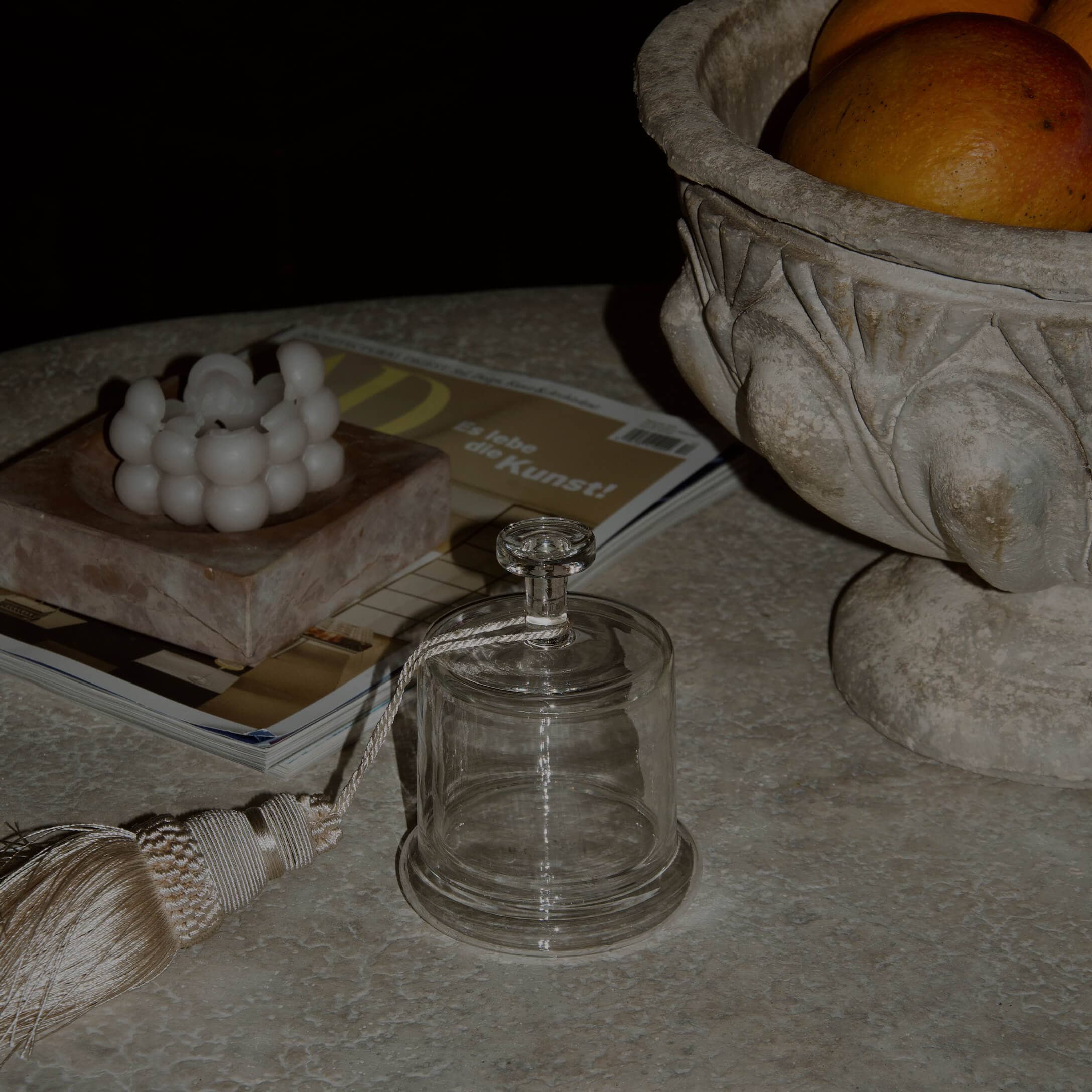 Cloche en verre transparent avec pompon décoratif sur table en marbre avec bougie et coupe en pierre