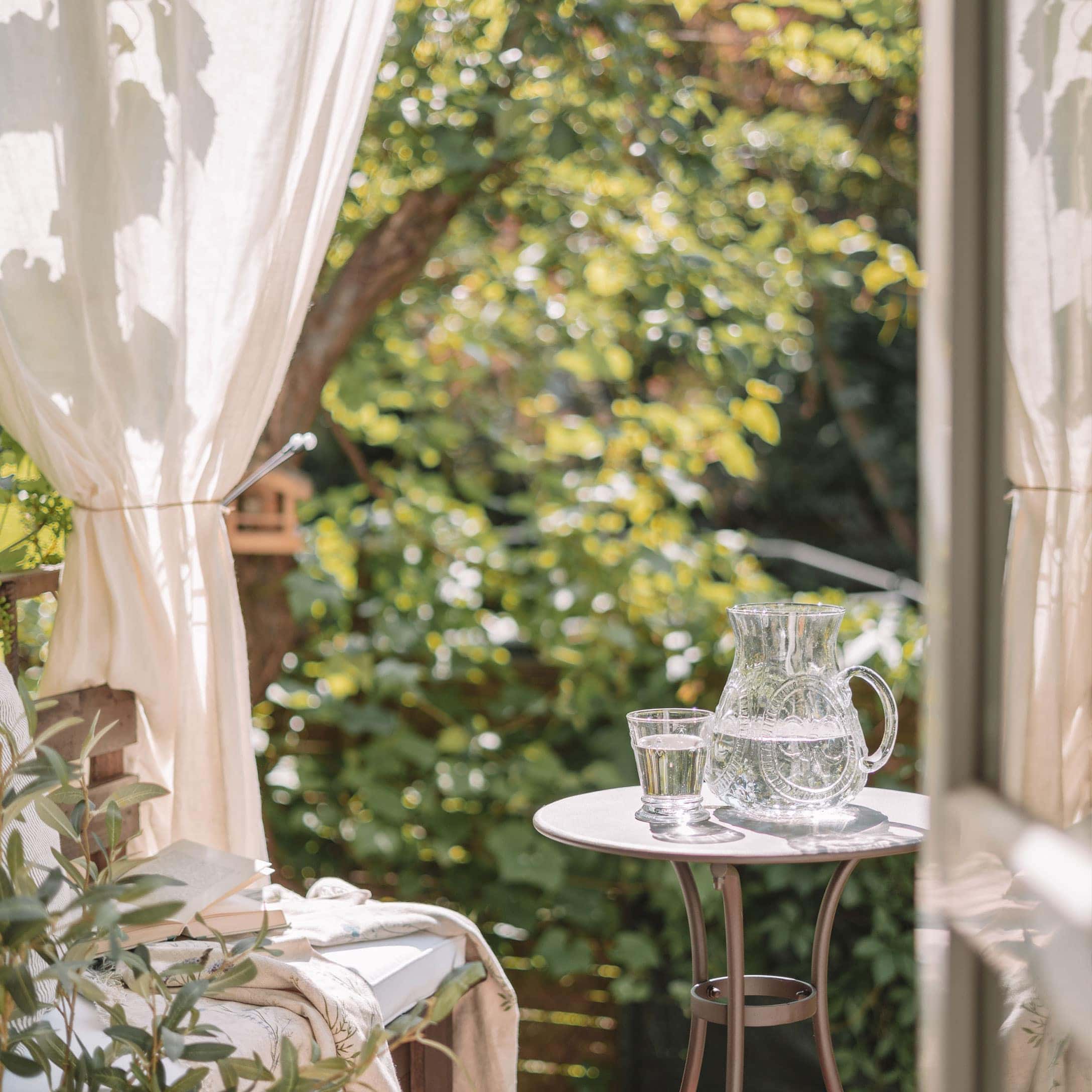 Carafe et verre en verre avec de l'eau sur une table blanche sur une terrasse verdoyante