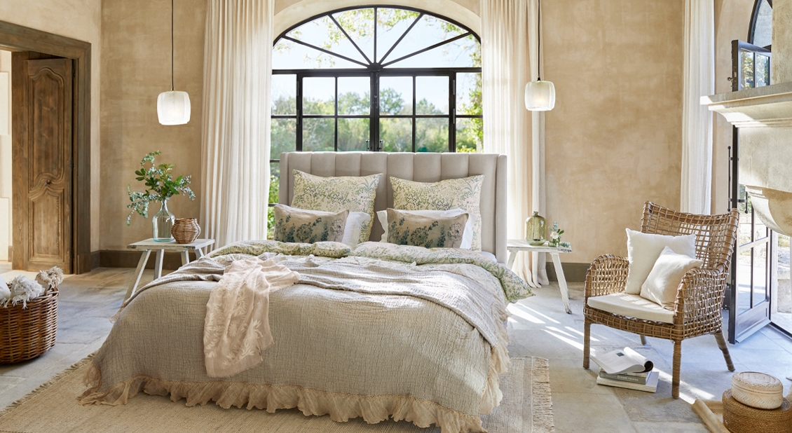Chambre chaleureuse avec literie beige et fauteuil en osier dans des tons naturels, style rustique