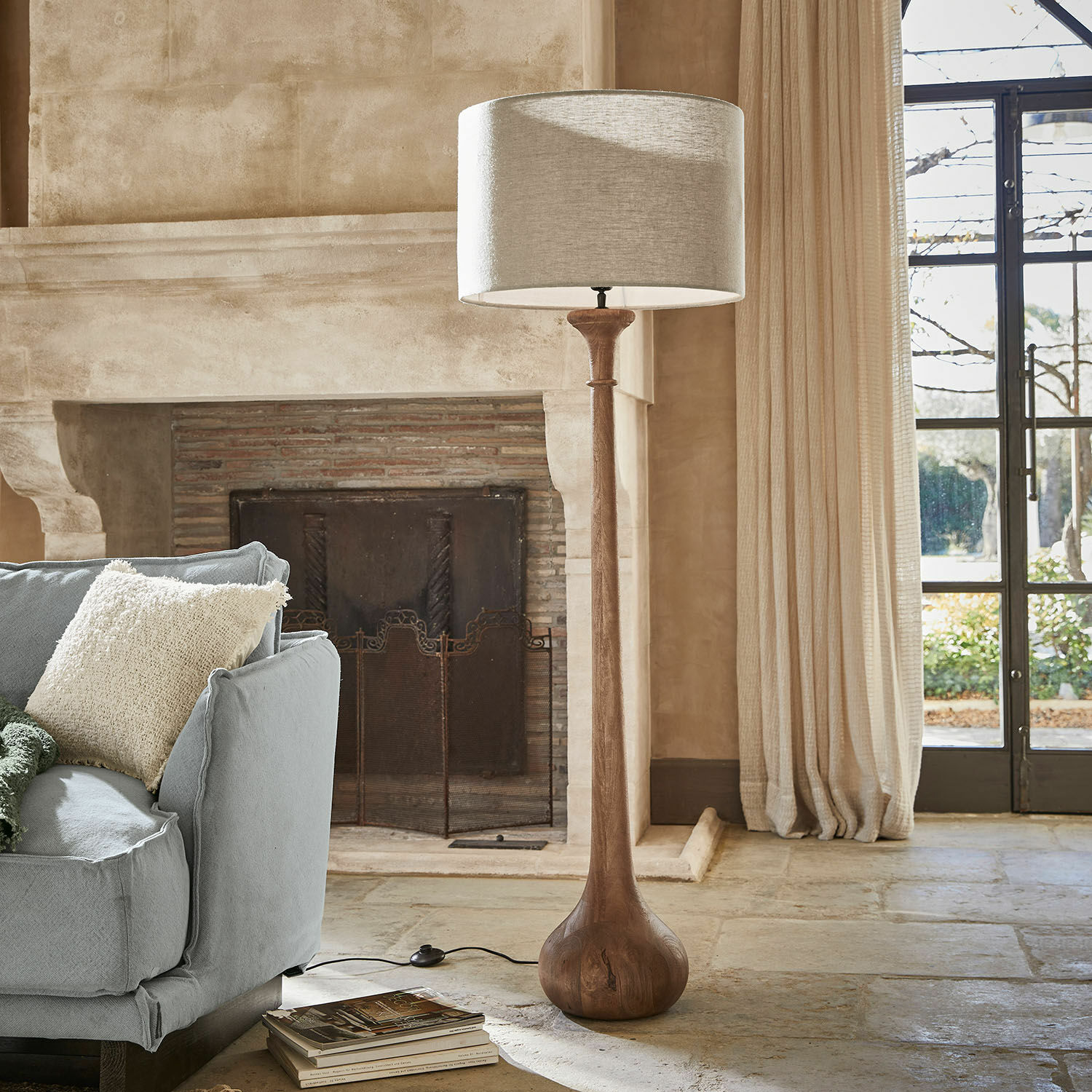 Lampe sur pied Andrées Lampadaire en bois avec abat-jour beige dans un salon chaleureux avec cheminée et canapé bleu