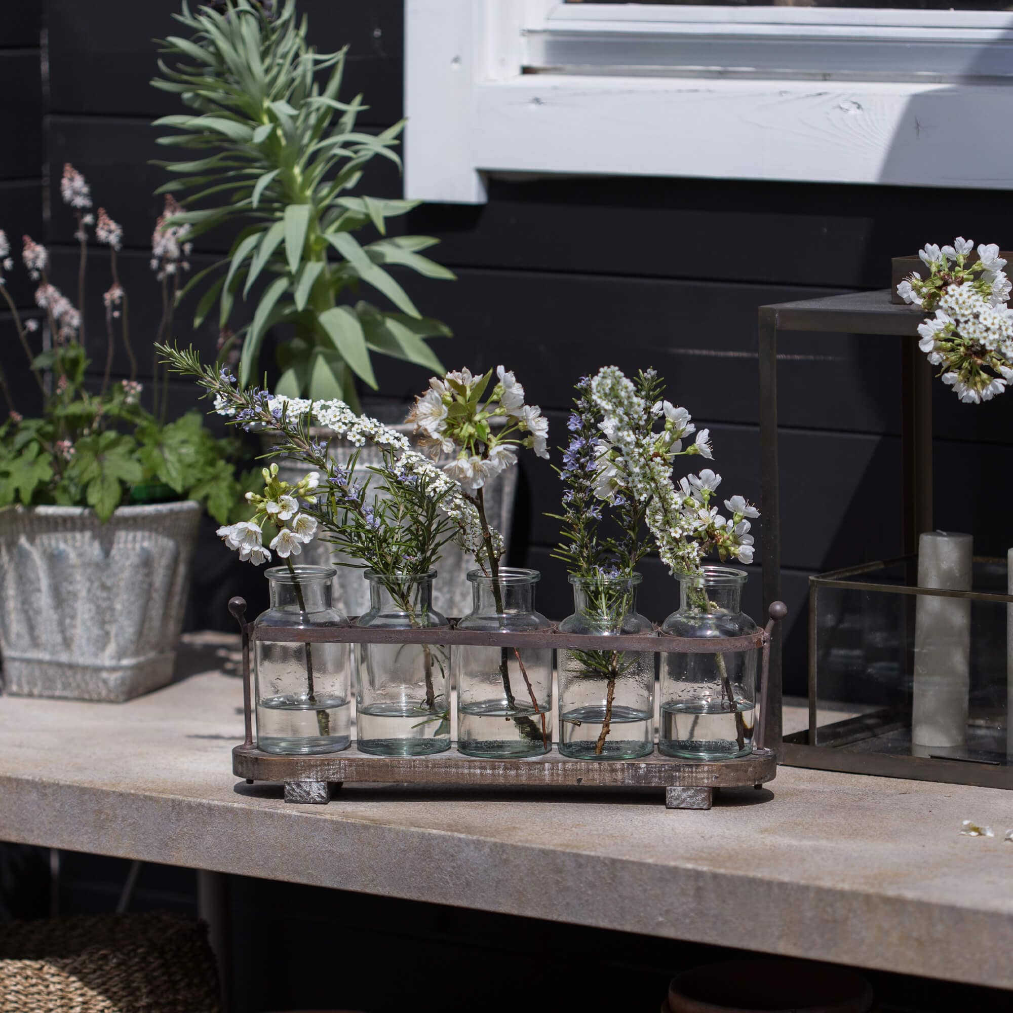 Bouteilles en verre avec fleurs blanches dans un support métallique sur une table en pierre, décoration extérieure