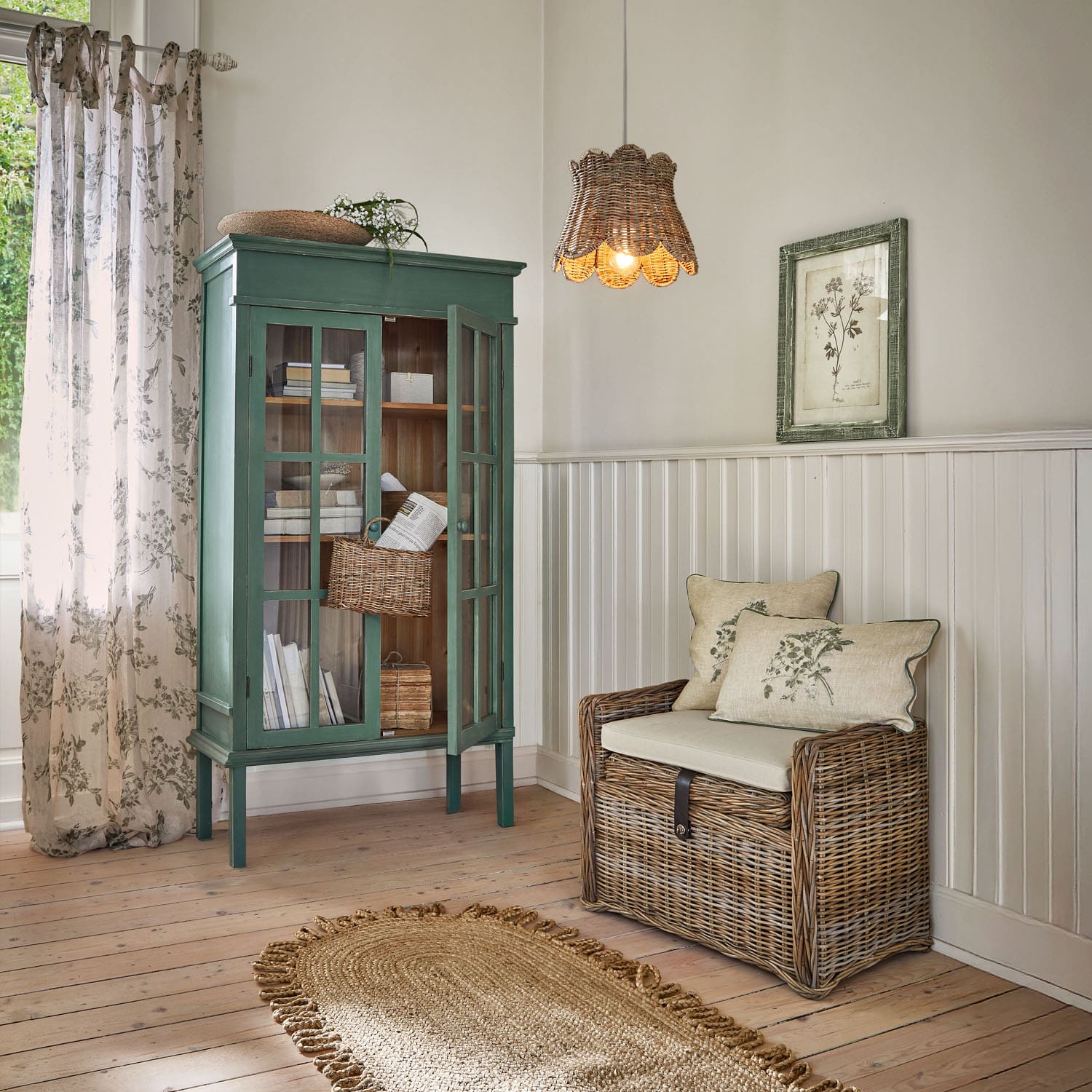 Vitrine en bois verte et banc en rotin avec coussins dans un salon clair avec tapis naturel