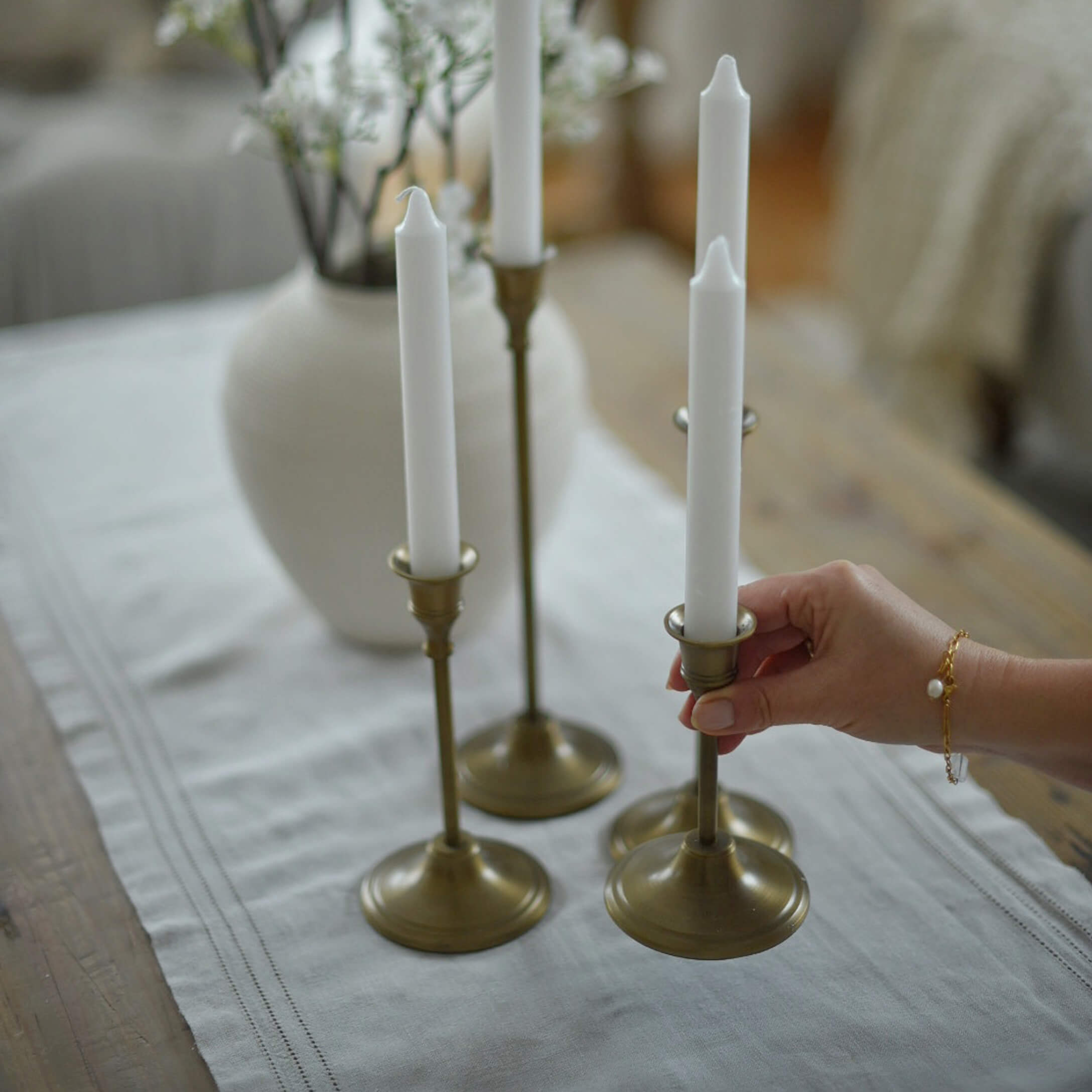 Ensemble de quatre bougeoirs en laiton avec bougies blanches sur une nappe en lin dans un intérieur chaleureux