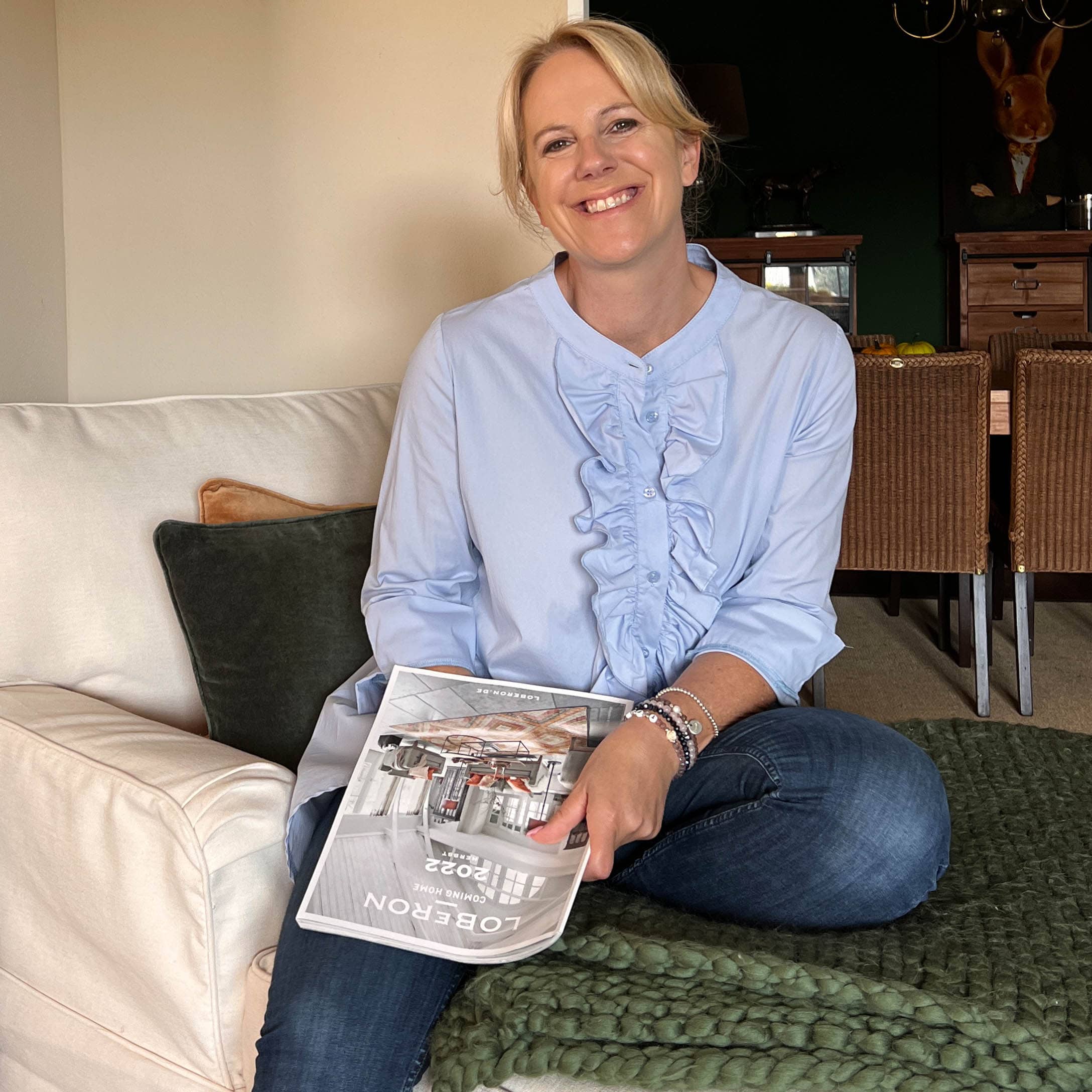 Femme assise sur un canapé avec un magazine Loberon, intérieur cosy avec couverture et coussins