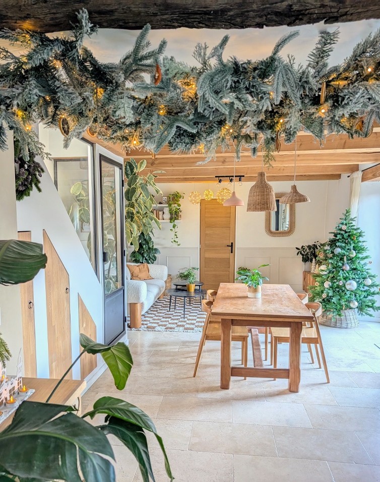 Intérieur chaleureux avec table en bois, sapin de Noël et décoration de branches vertes illuminées par des LED