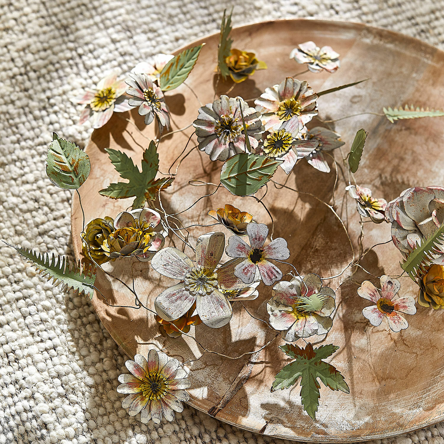 Guirlande Urfanne Fleurs et feuilles décoratives en métal aux couleurs pastel sur un plateau en bois, décoration intérieure