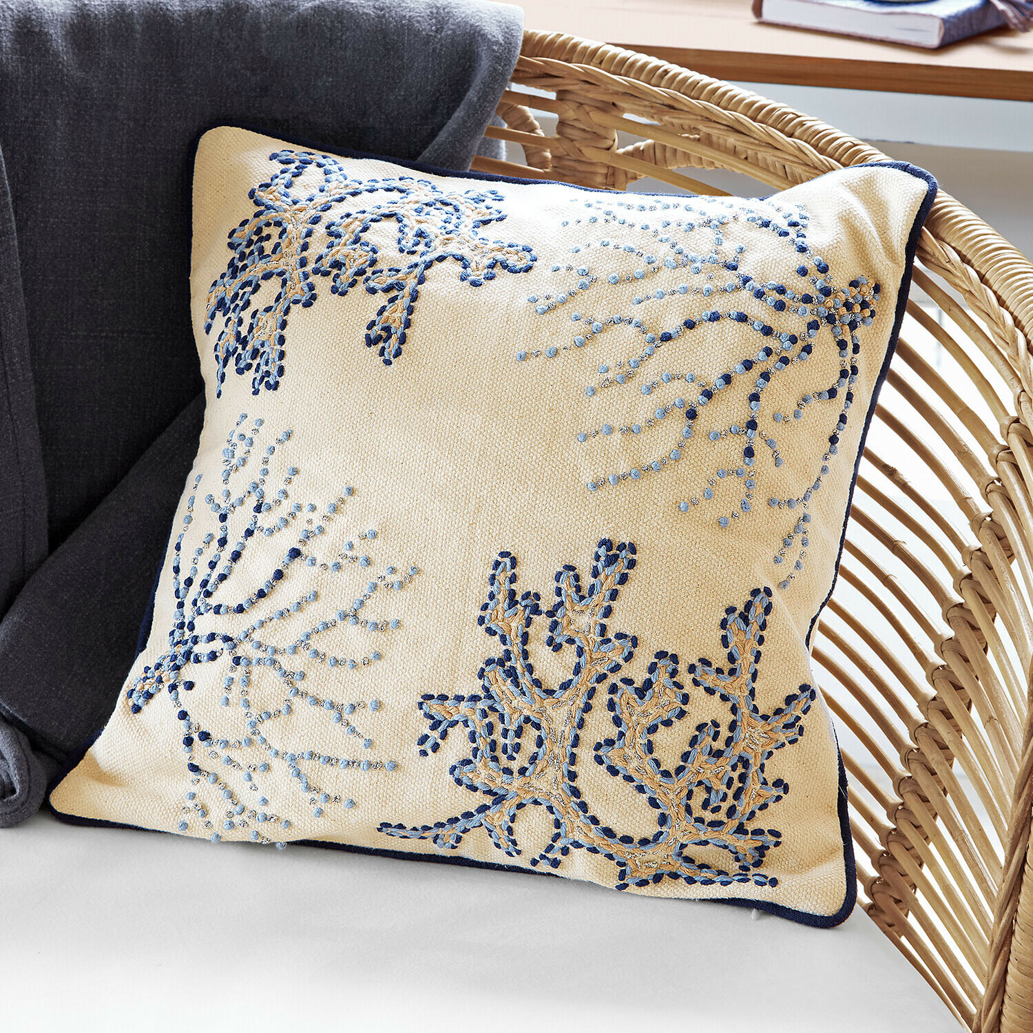 Housse de coussin Whitmere Coussin beige décoratif avec broderie bleue et bordure marine sur fauteuil en osier