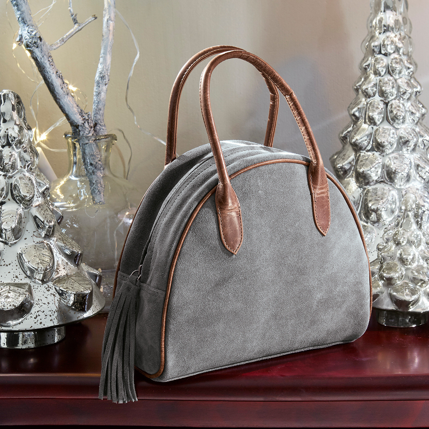 Sac Elisabeta Sac en daim gris avec poignées en cuir marron et franges posé sur une table avec décorations de Noël