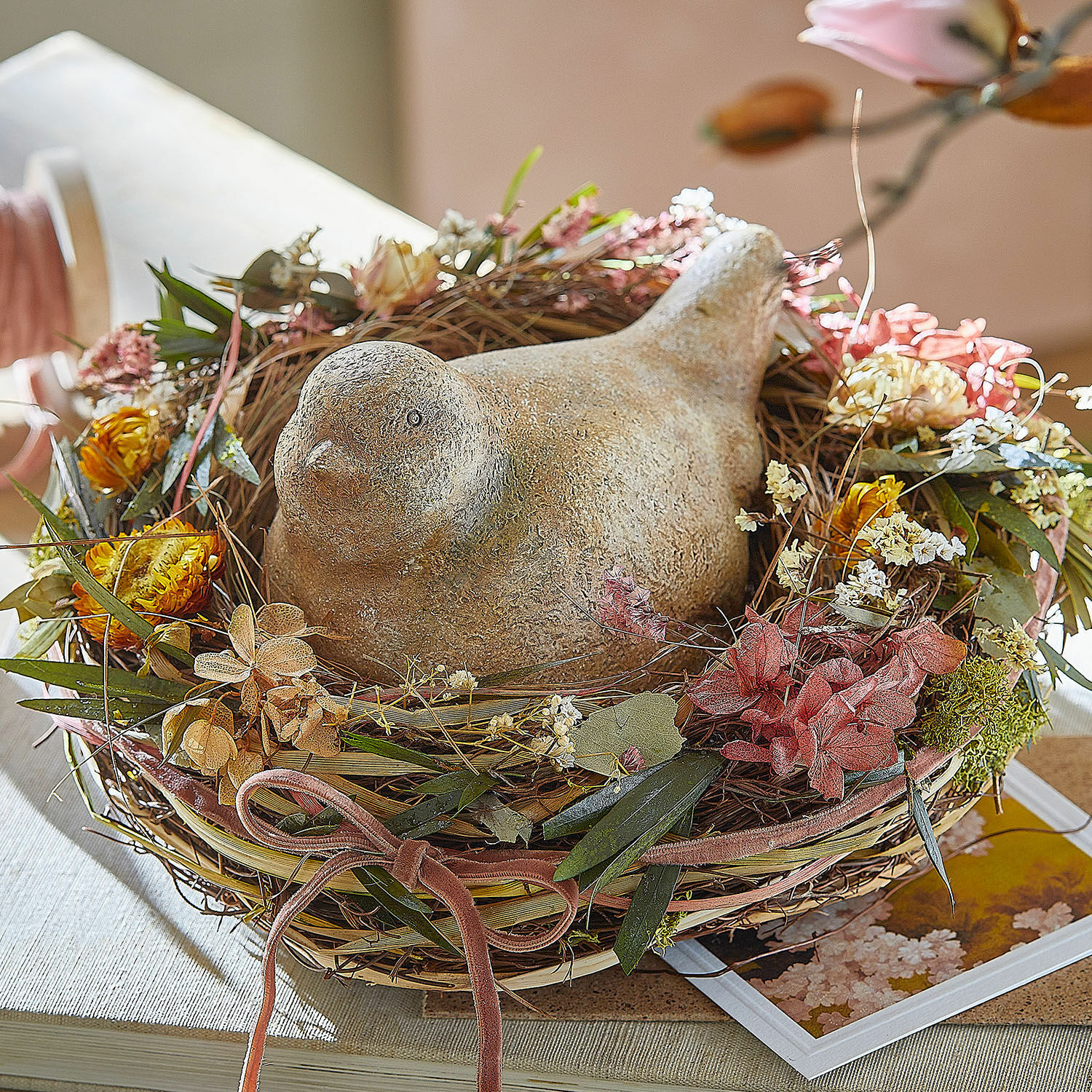 Figurine décorative Nafisah Oiseau décoratif en pierre dans un nid en osier avec fleurs séchées sur une table