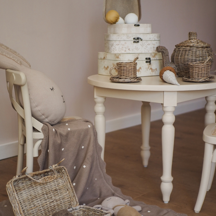 Table beige avec service à thé en osier et boîtes décoratives dans une chambre d'enfant chaleureuse