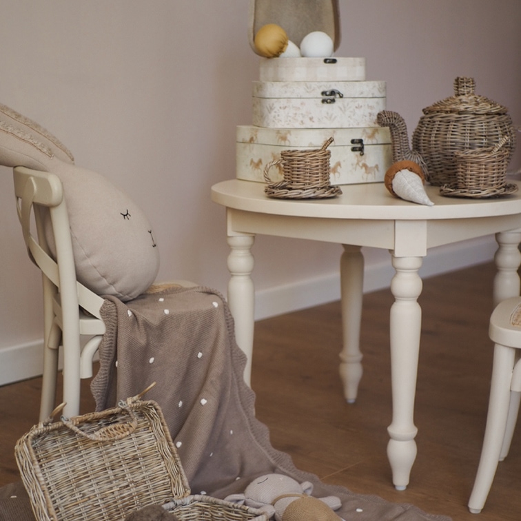 Table beige avec service à thé en osier et boîtes décoratives dans une chambre d'enfant chaleureuse