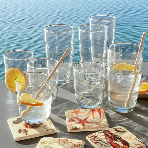 Verres en verre transparent avec tranches de citron et touilleurs en bois, sous-verres à motifs marins au bord de l'eau