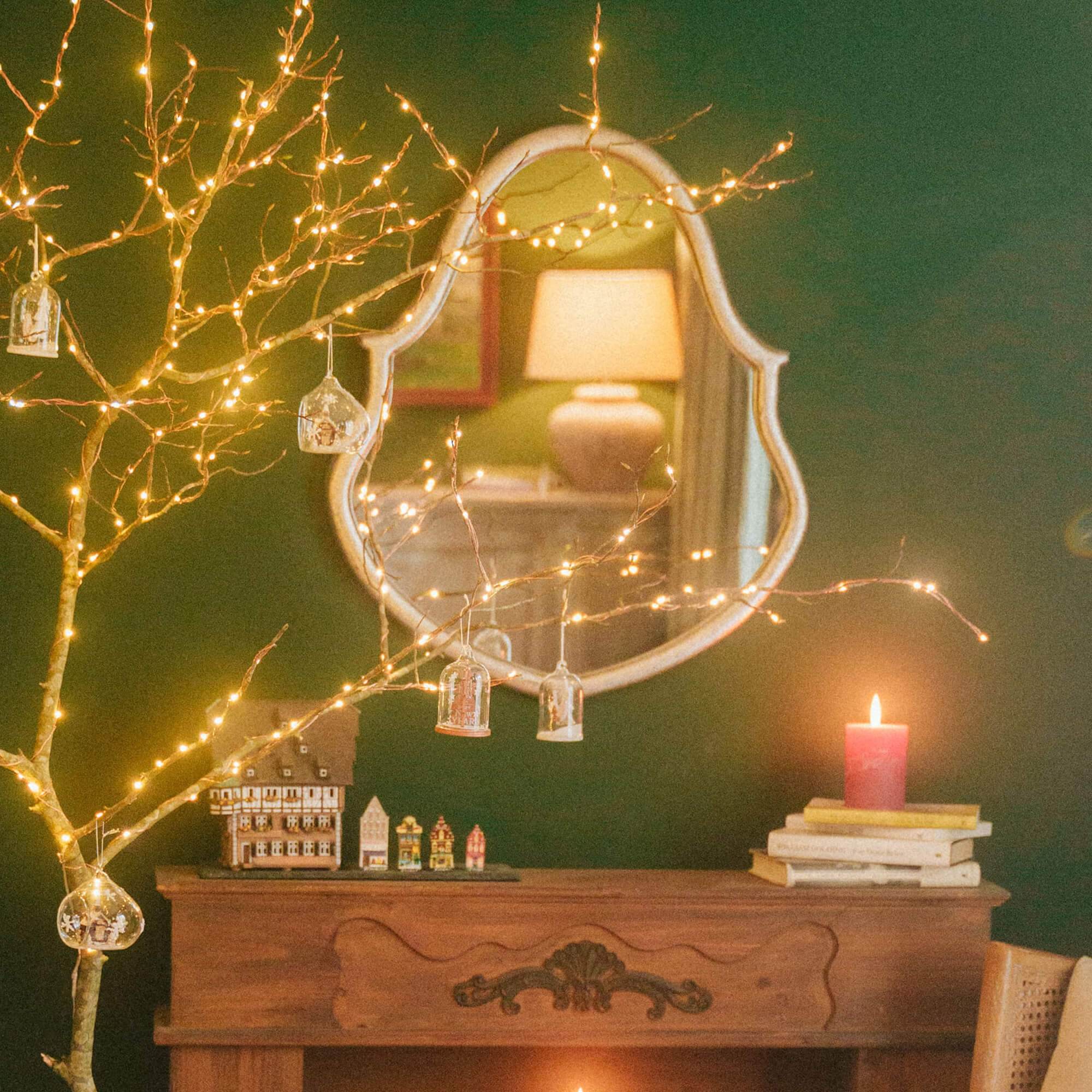 Décoration de Noël avec branches lumineuses et bougie rouge sur une cheminée en bois dans un salon