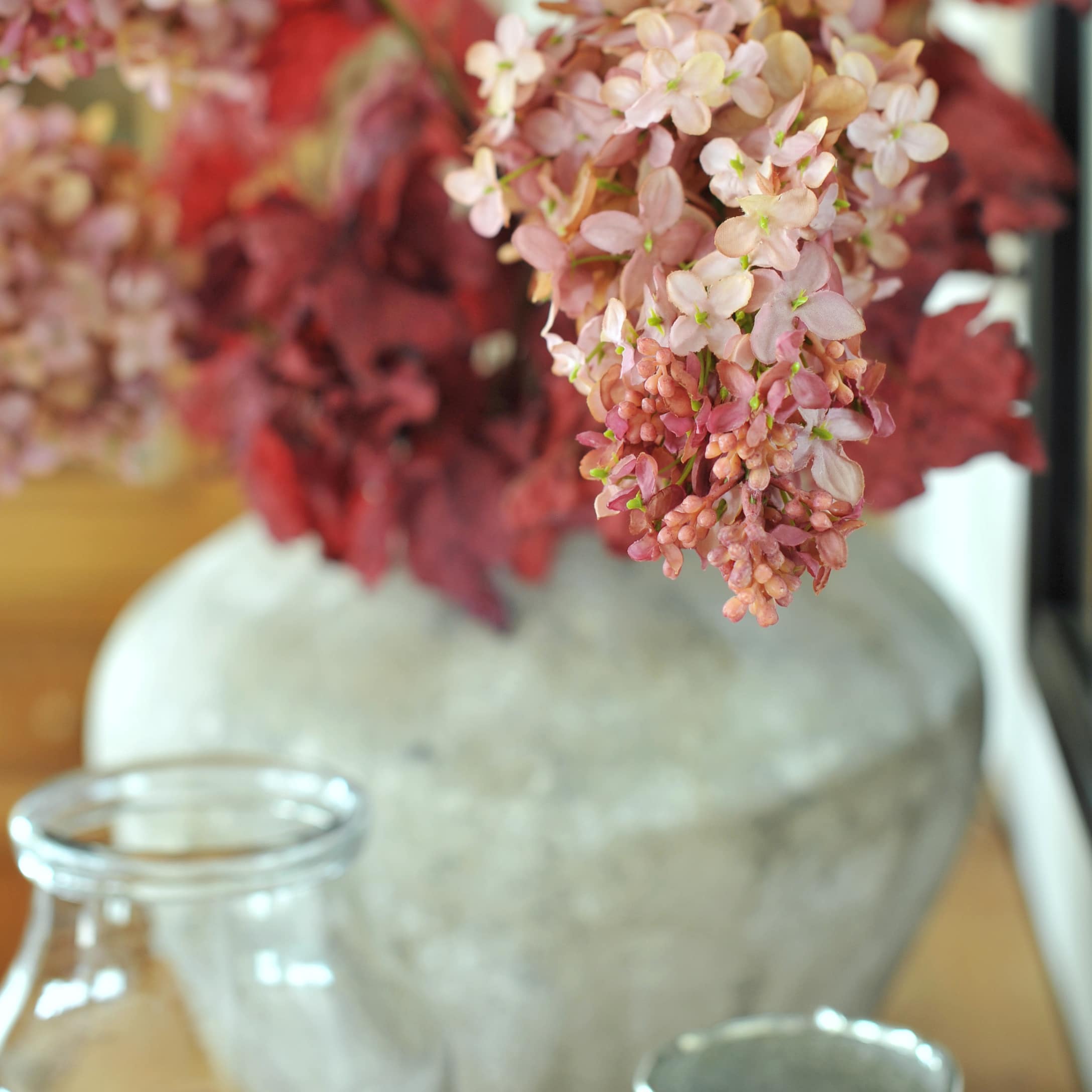 Vase décoratif en pierre avec fleurs roses et feuilles rouges sur une table dans un salon