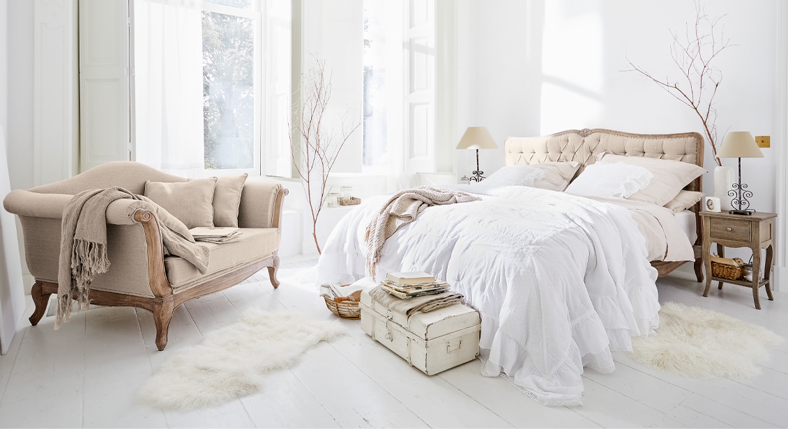 Chambre chaleureuse avec lit capitonné beige et canapé vintage sur parquet en bois clair