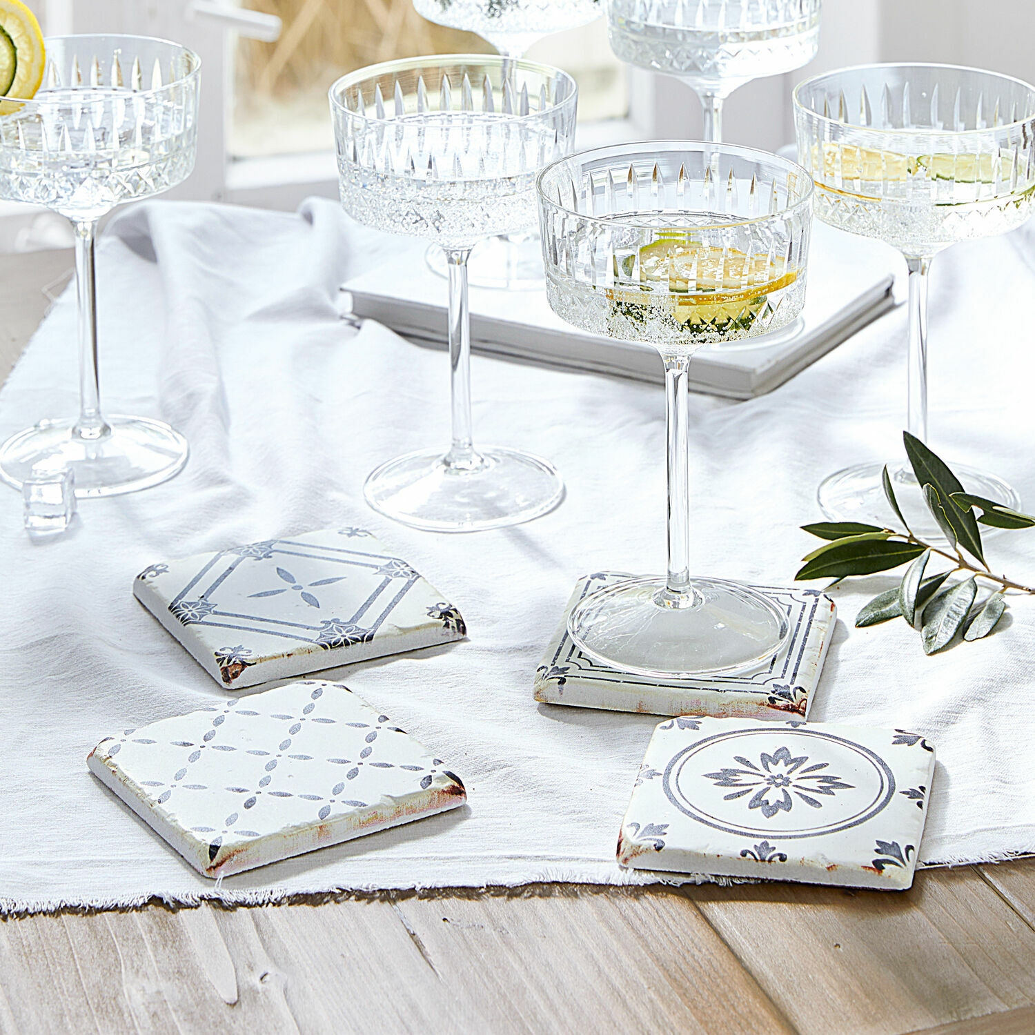 Lot de 4 dessous de verres Emma Ensemble de sous-verres en céramique blanche et grise avec motifs, posés sur une table en bois clair