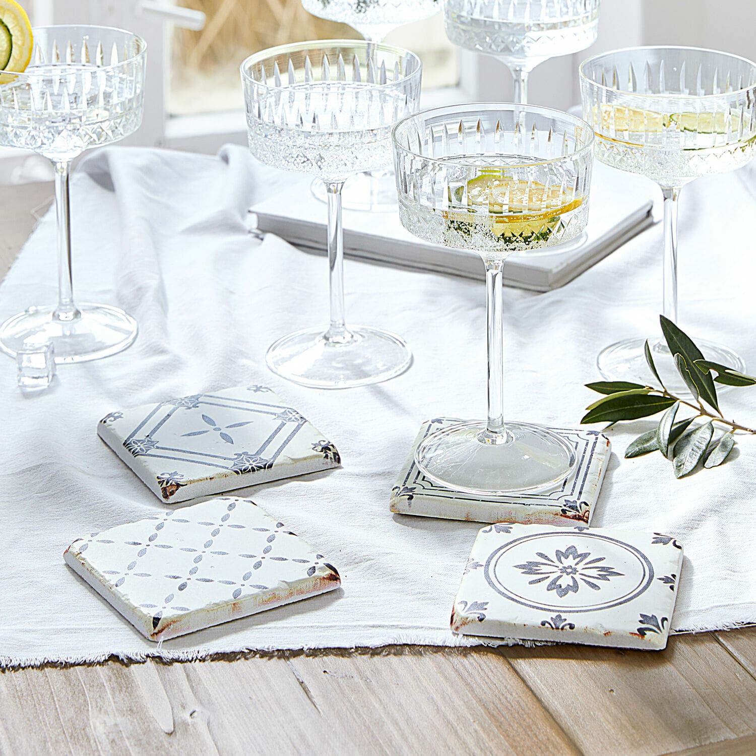 Lot de 4 dessous de verres Emma Ensemble de sous-verres en céramique blanche et grise avec motifs, posés sur une table en bois clair