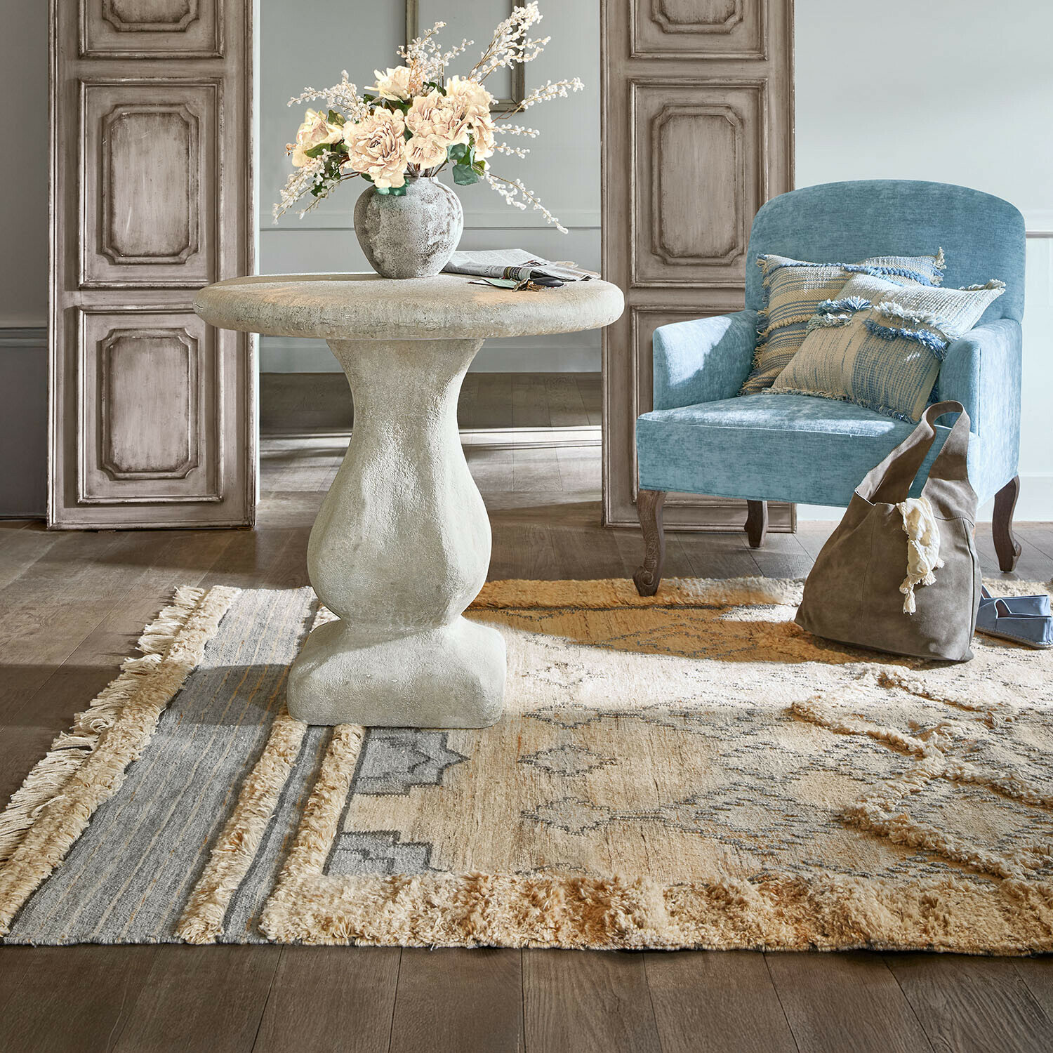 Tapis d'intérieur et d'extérieur Ciel d'Azur Table ronde en béton gris avec vase fleuri près d'un fauteuil bleu et tapis décoratif