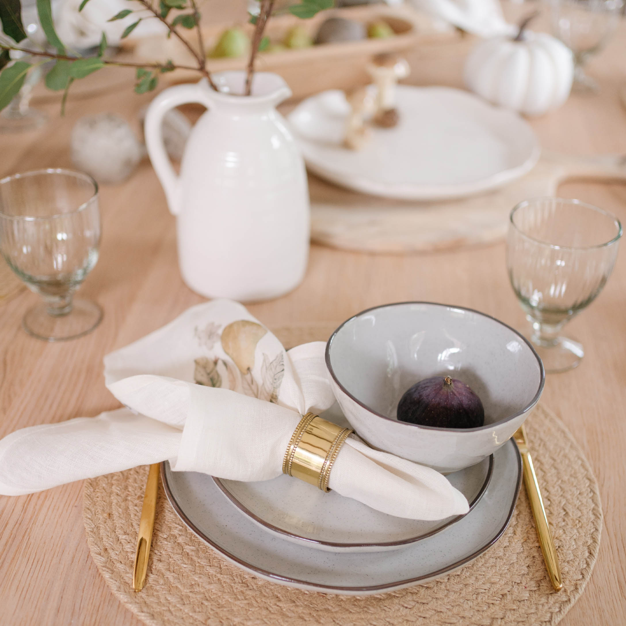 Service de table en céramique gris clair avec couverts dorés et serviette en lin sur napperon naturel