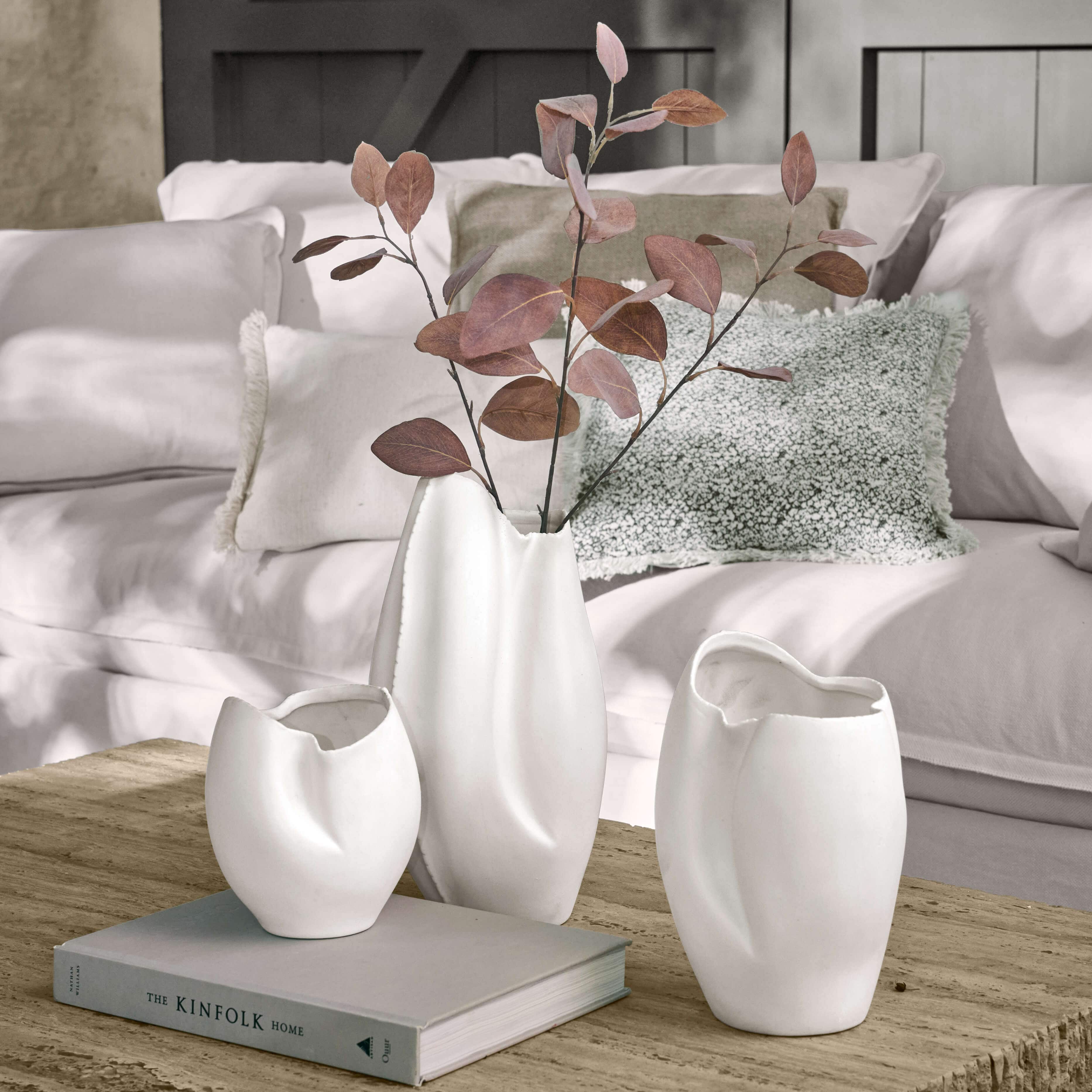 Ensemble de trois vases en céramique blanche aux formes irrégulières sur une table en bois dans un salon