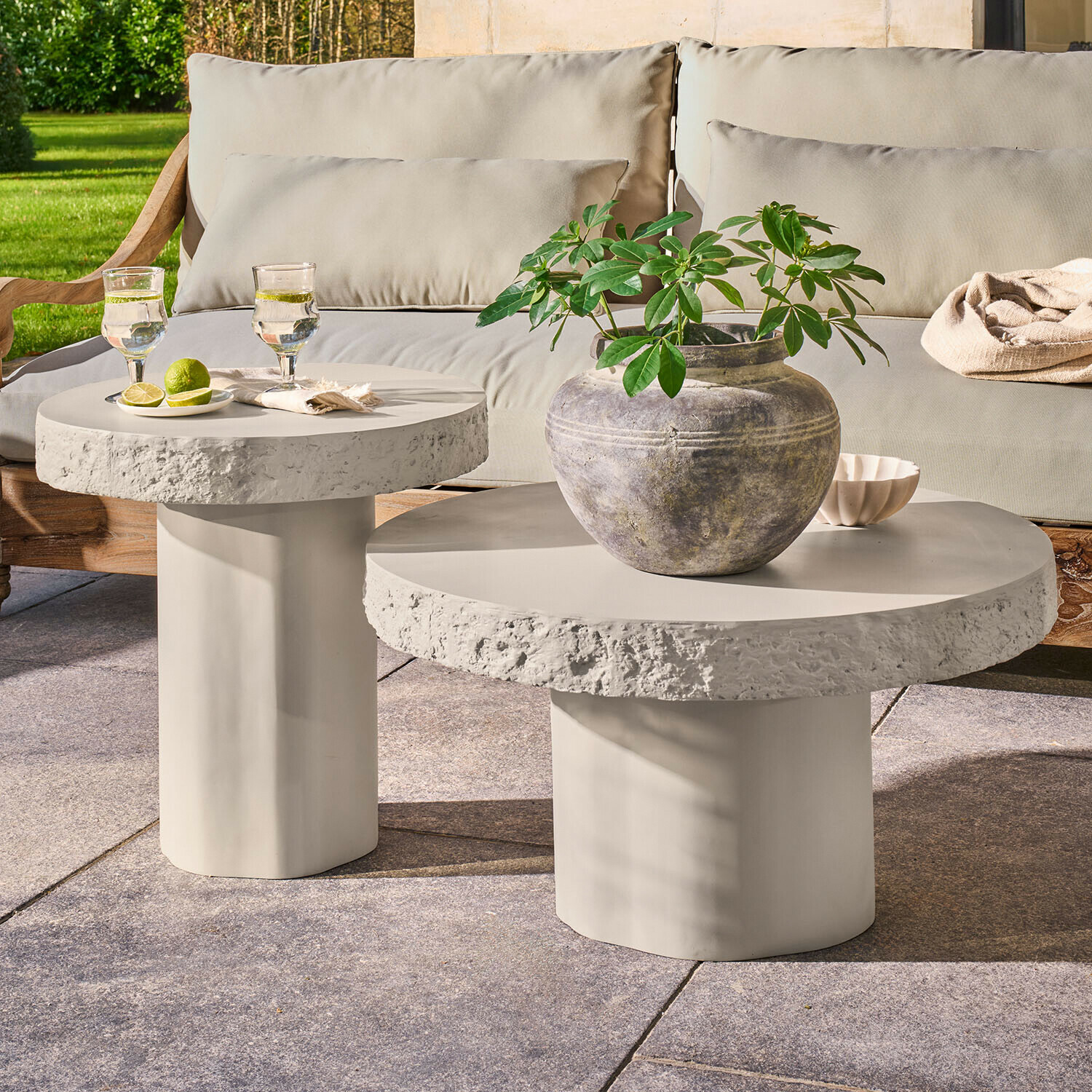 Ensemble de deux tables basses rondes en béton gris clair sur terrasse avec plante et verres d'eau