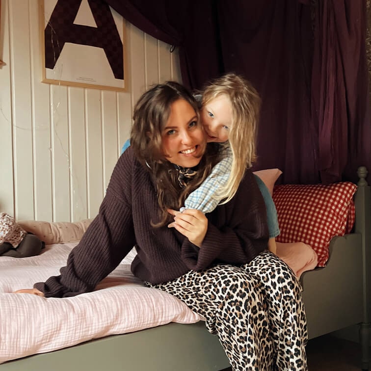 Femme en pull marron et pantalon léopard assise sur un lit avec un enfant en chemise à carreaux claire
