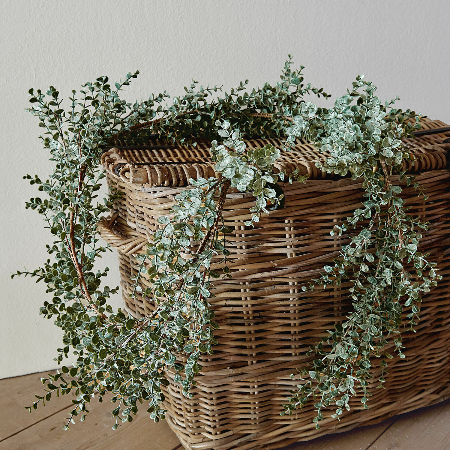 Guirlande Valerie Couronne décorative de feuilles vertes posée sur un panier en osier sur un sol en bois