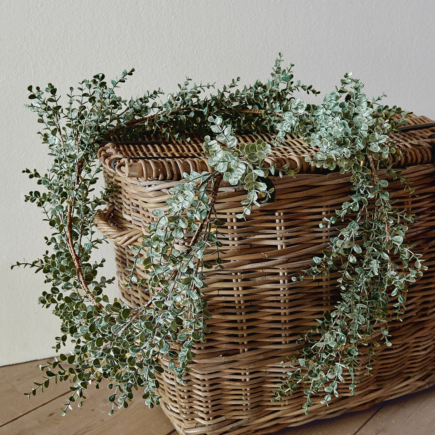 Guirlande Valerie Couronne décorative de feuilles vertes posée sur un panier en osier sur un sol en bois