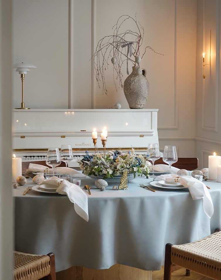 Table élégamment dressée avec nappe bleue et centre floral dans un salon clair avec piano blanc