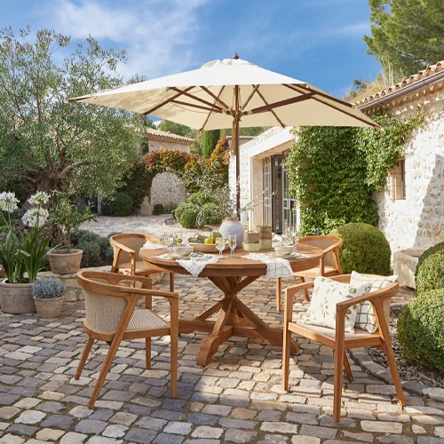 Table de jardin en bois avec parasol et quatre chaises sur pavés dans une cour ensoleillée