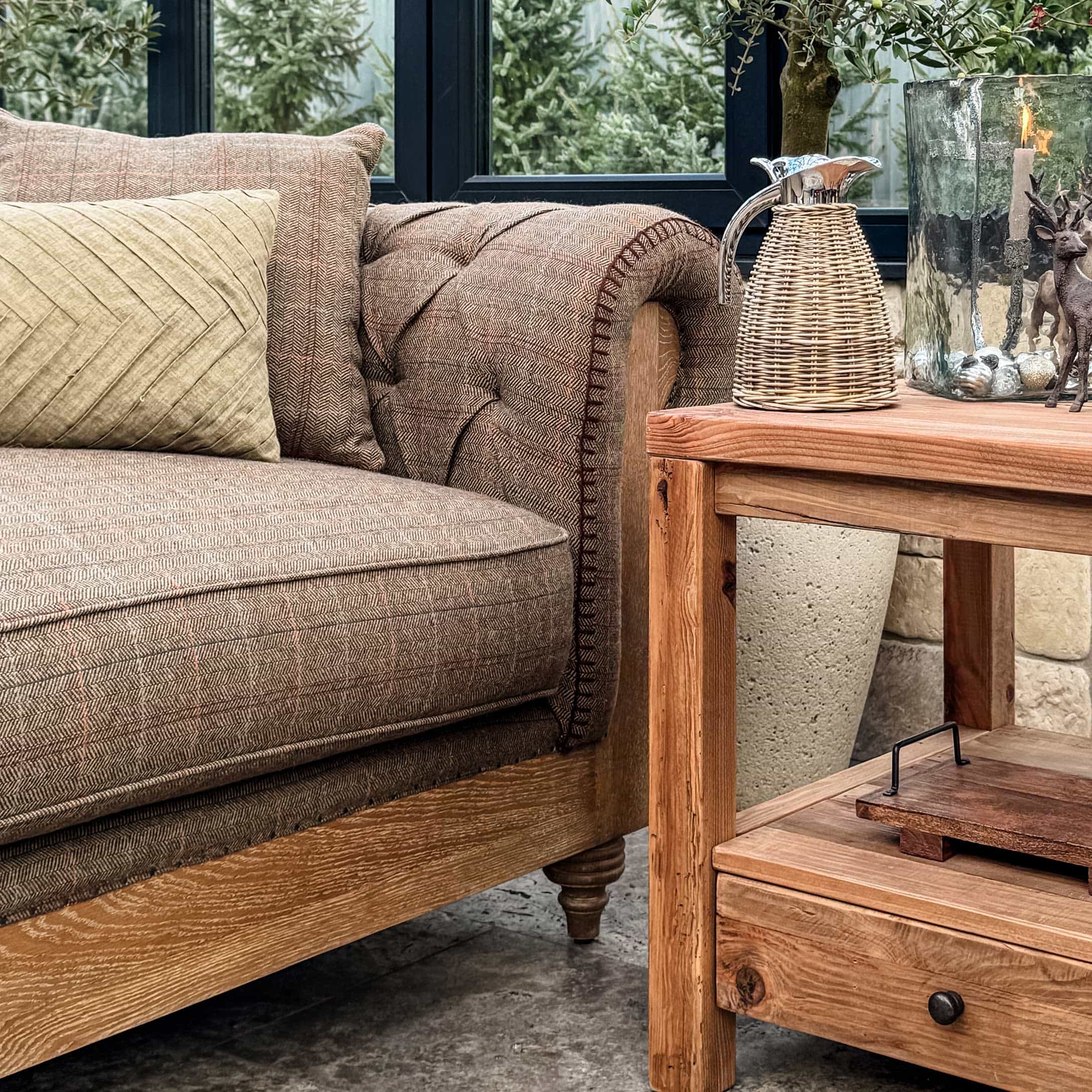 Canapé en tissu marron avec structure en bois à côté d'une table en bois décorée pour Noël en véranda