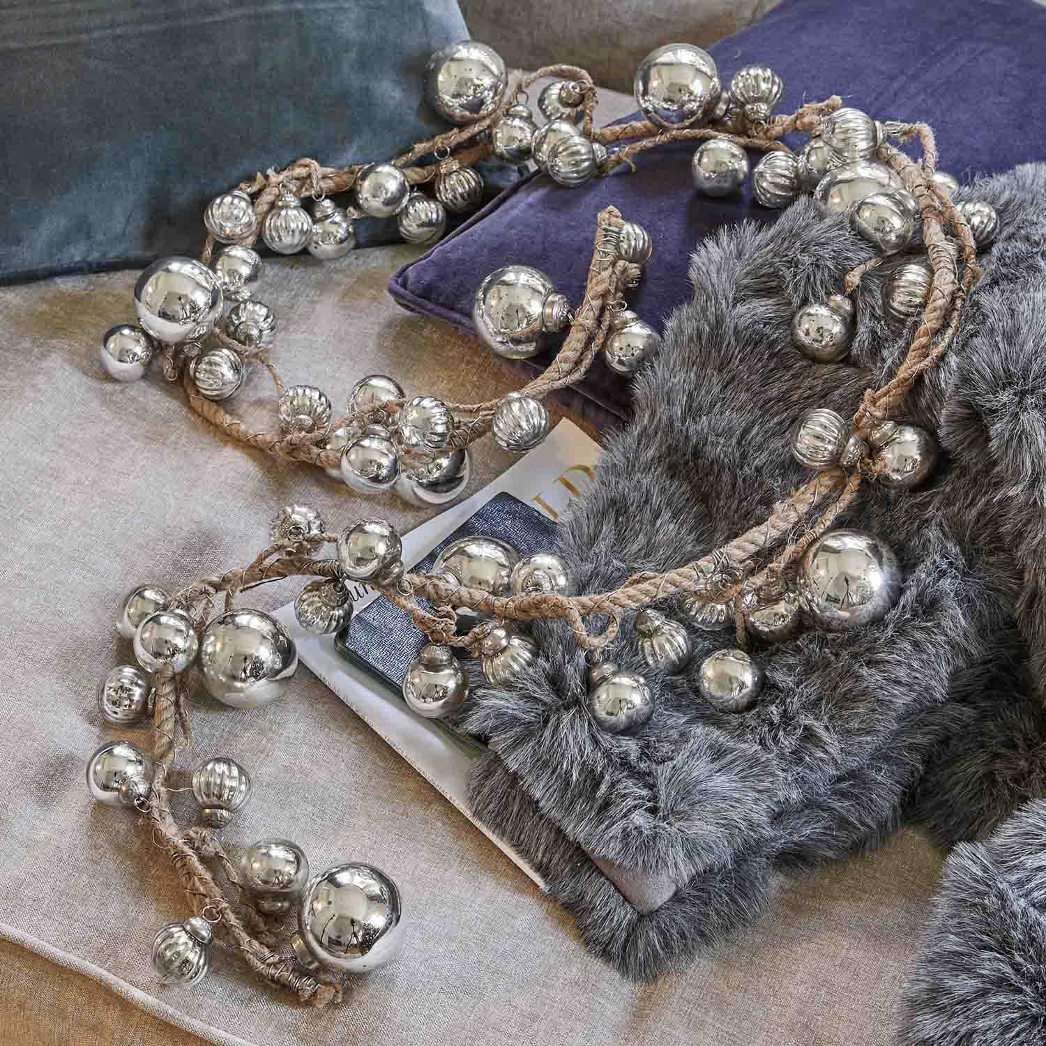 Guirlande décorative avec boules métalliques argentées sur corde en jute posée sur coussins doux et fausse fourrure