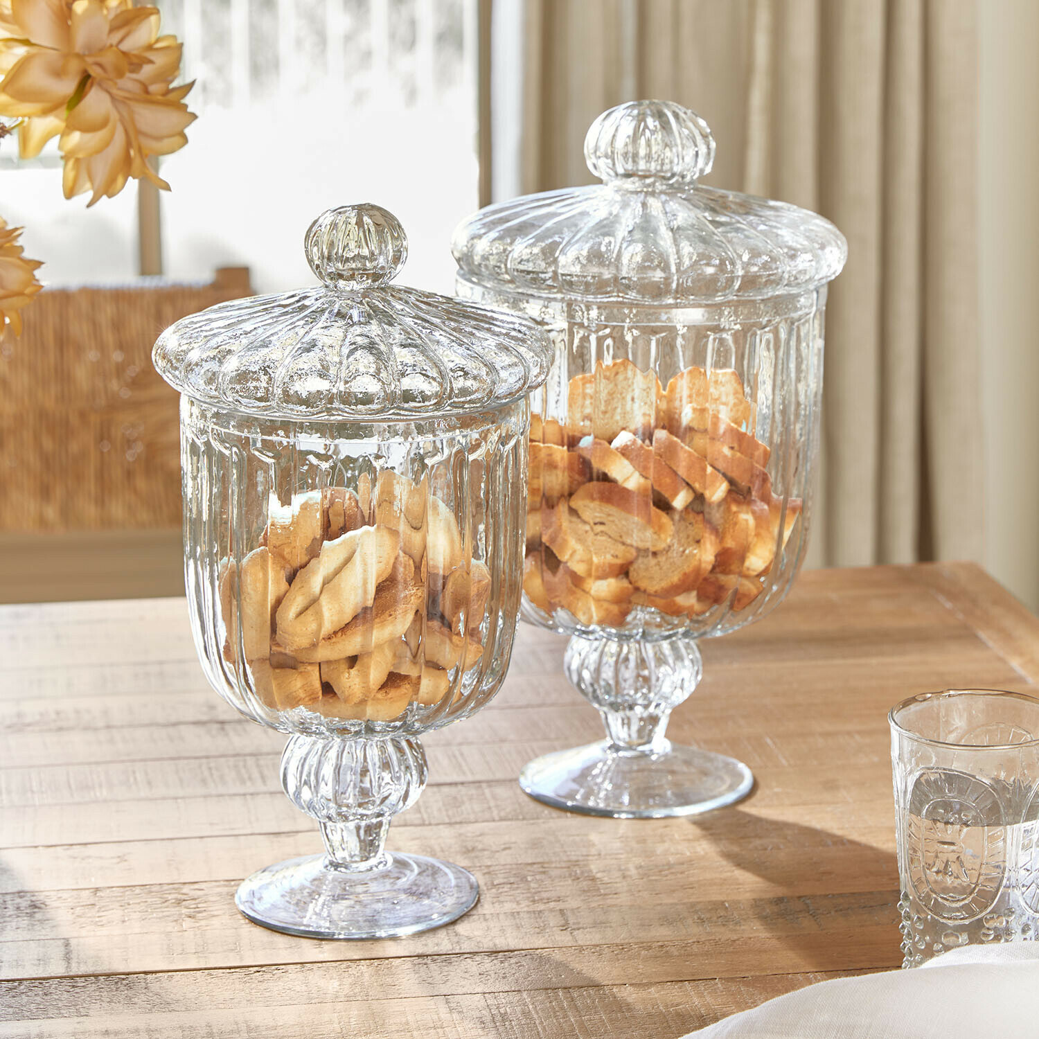 Lot de 2 bonbonnières en verre Mélomiane Deux bocaux en verre transparent avec couvercles remplis de biscuits sur une table en bois clair