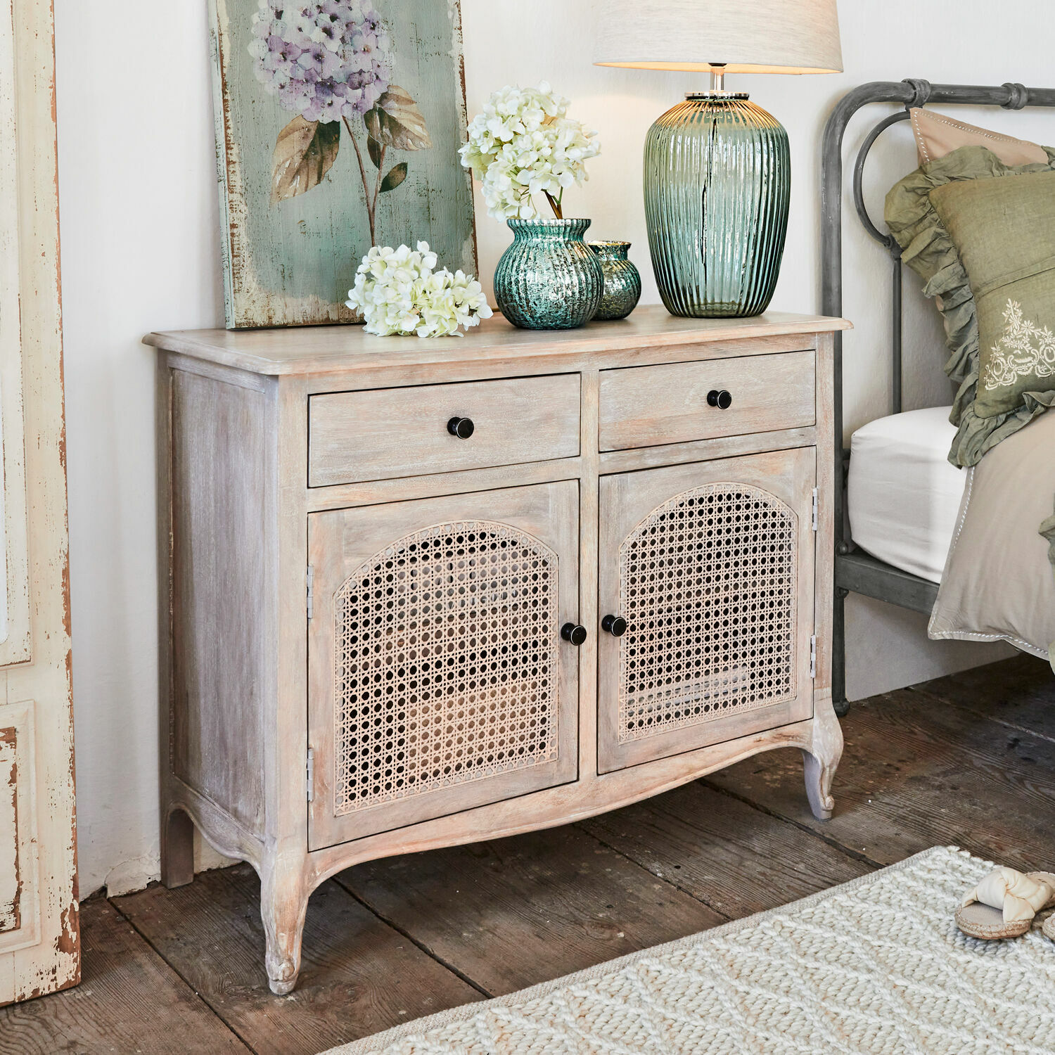 Commode Truso Commode en bois clair avec portes en cannage, décorations et lampe posées dessus