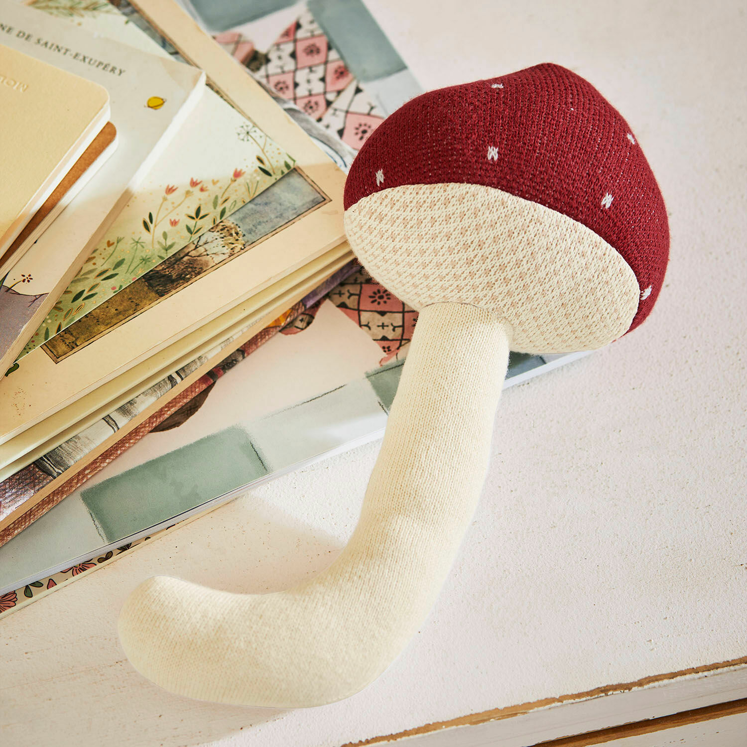 Peluche Norilie Jouet en peluche en forme de champignon rouge et crème posé sur une table avec des livres