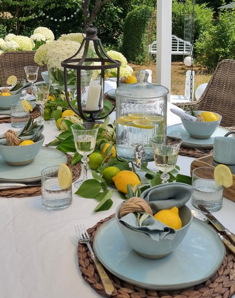 Table d'été en extérieur avec vaisselle bleue, citrons et carafe en verre d'eau citronnée