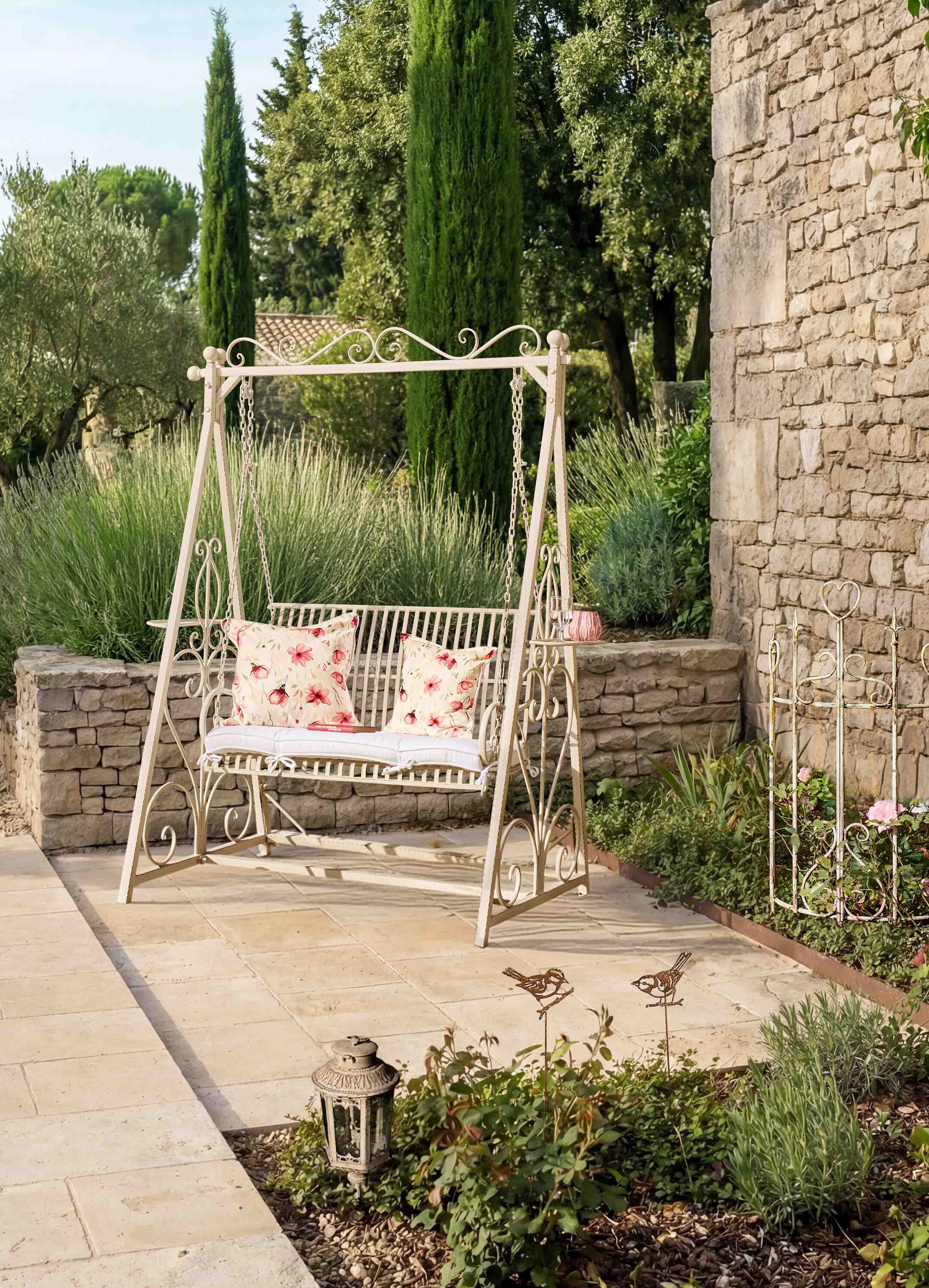 Balançoire de jardin en métal crème avec coussins à motifs floraux sur terrasse en pierre naturelle